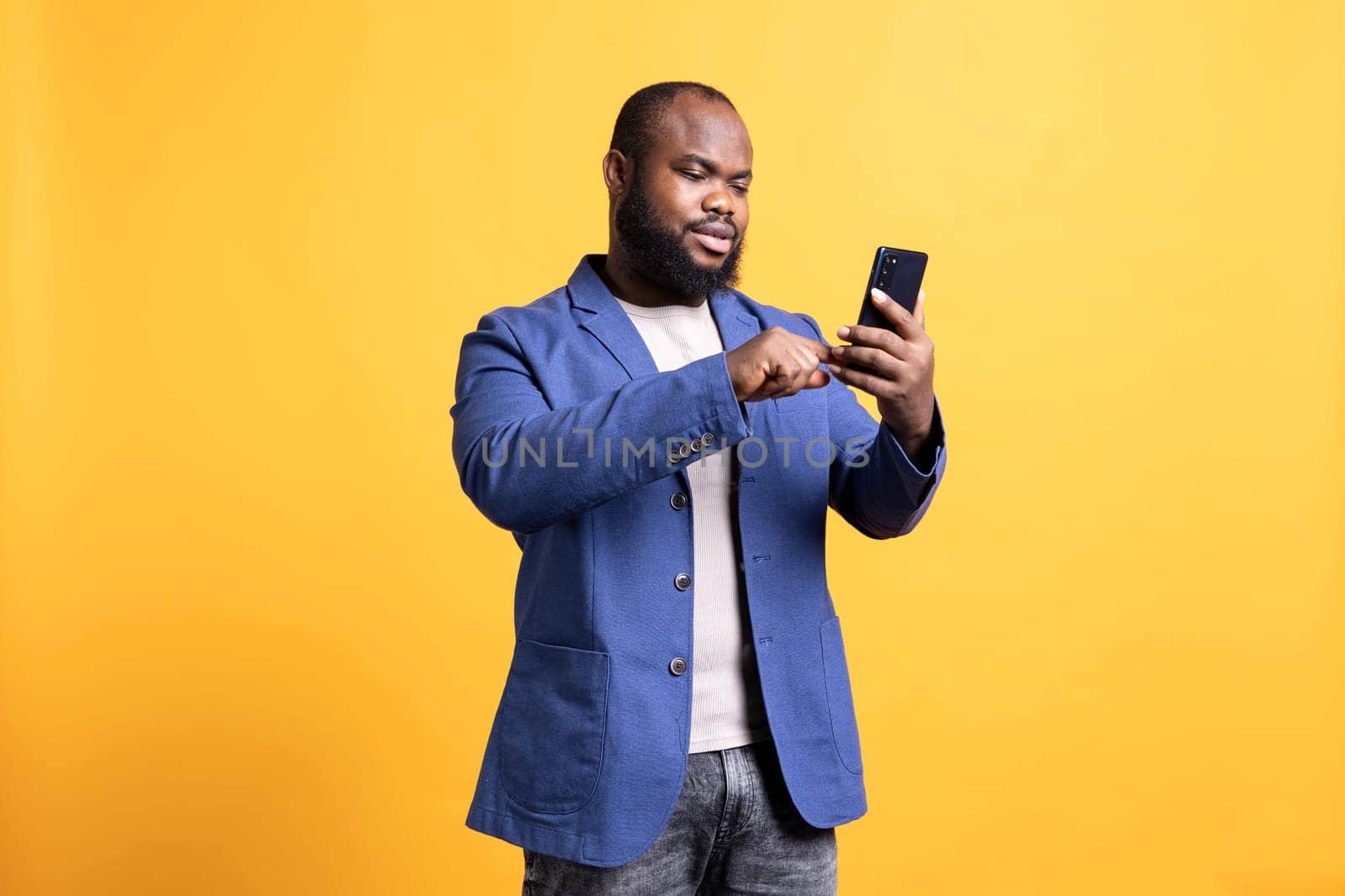 Man scrolling on smartphone touchscreen, using mobile phone to check social media feed. African american person browsing internet websites, isolated over studio background