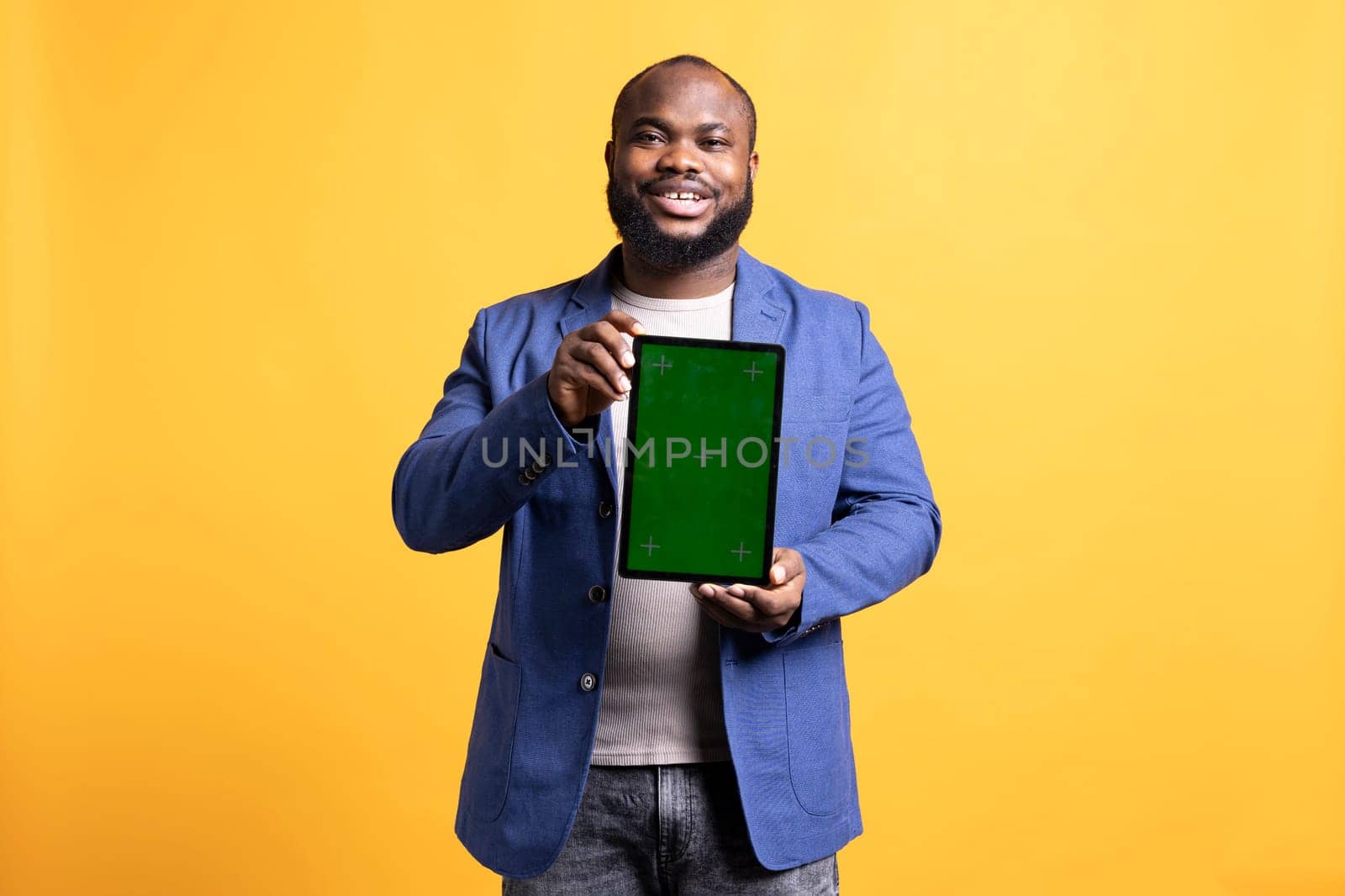 Smiling african american man presenting tablet with green screen display, isolated over studio background. Cheerful BIPOC person creating promotion with blank copy space mockup device