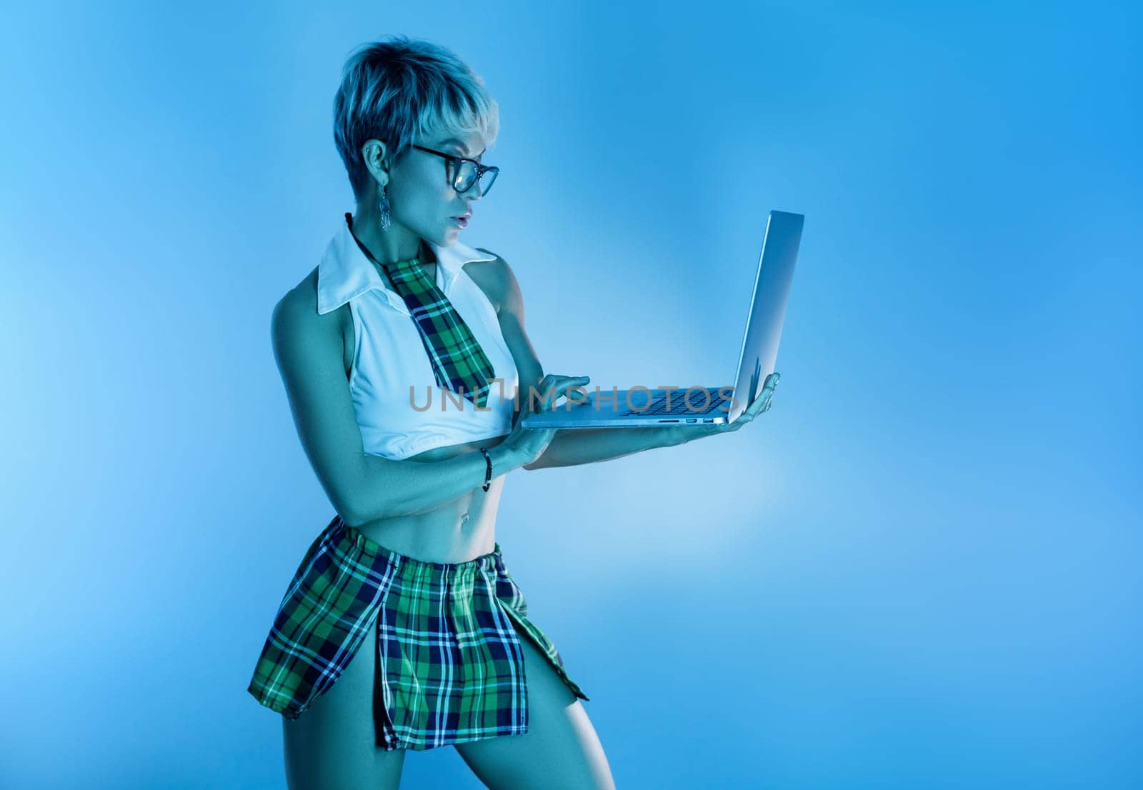 Sexy girl in glasses and an erotic school suit with a plaid skirt with a laptop in blue neon light on the background of a copy paste by Rotozey