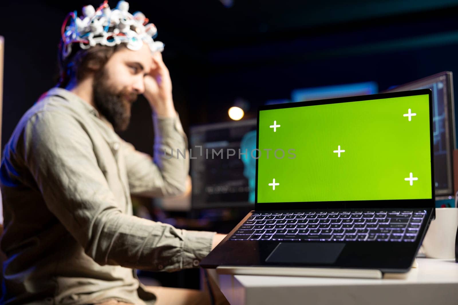 Focus on green screen laptop used by developer wearing EEG headset device translating thoughts into PC commands. IT professional controlling computer functions using mind, helped by mockup notebook