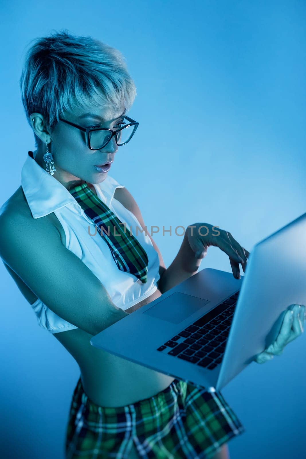 Sexy girl in glasses and an erotic school suit with a plaid skirt with a laptop in blue neon light on the background of a copy paste by Rotozey