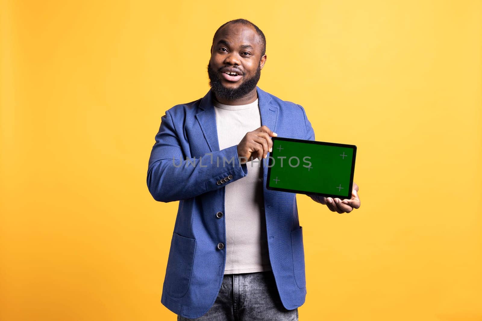 Jolly african american man presenting video on green screen tablet in landscape mode, studio background. Upbeat BIPOC person holding blank copy space chroma key device used for showcasing ads