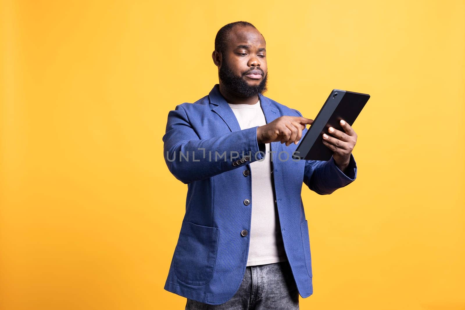 Bored person mindlessly scrolling on tablet screen, isolated over studio background. African american man passing time on social media on portable device, enjoying leisure time