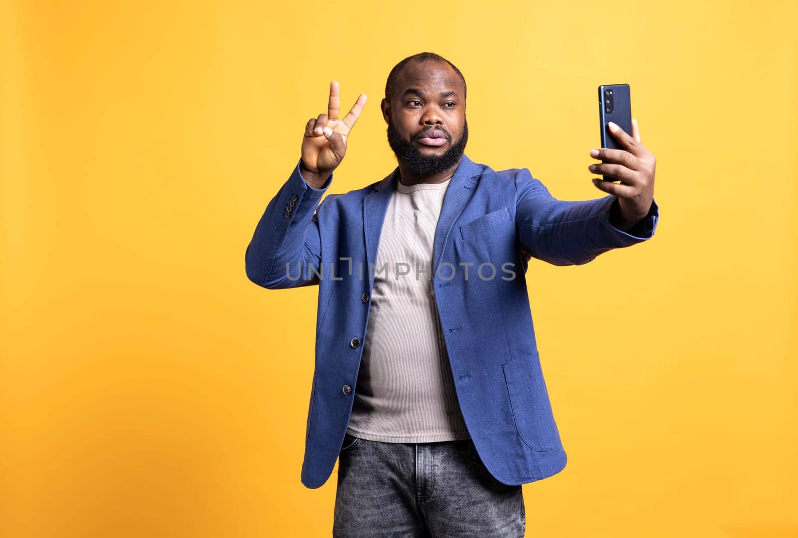 Man using smartphone to take selfies, doing victory hand sign, studio background by DCStudio
