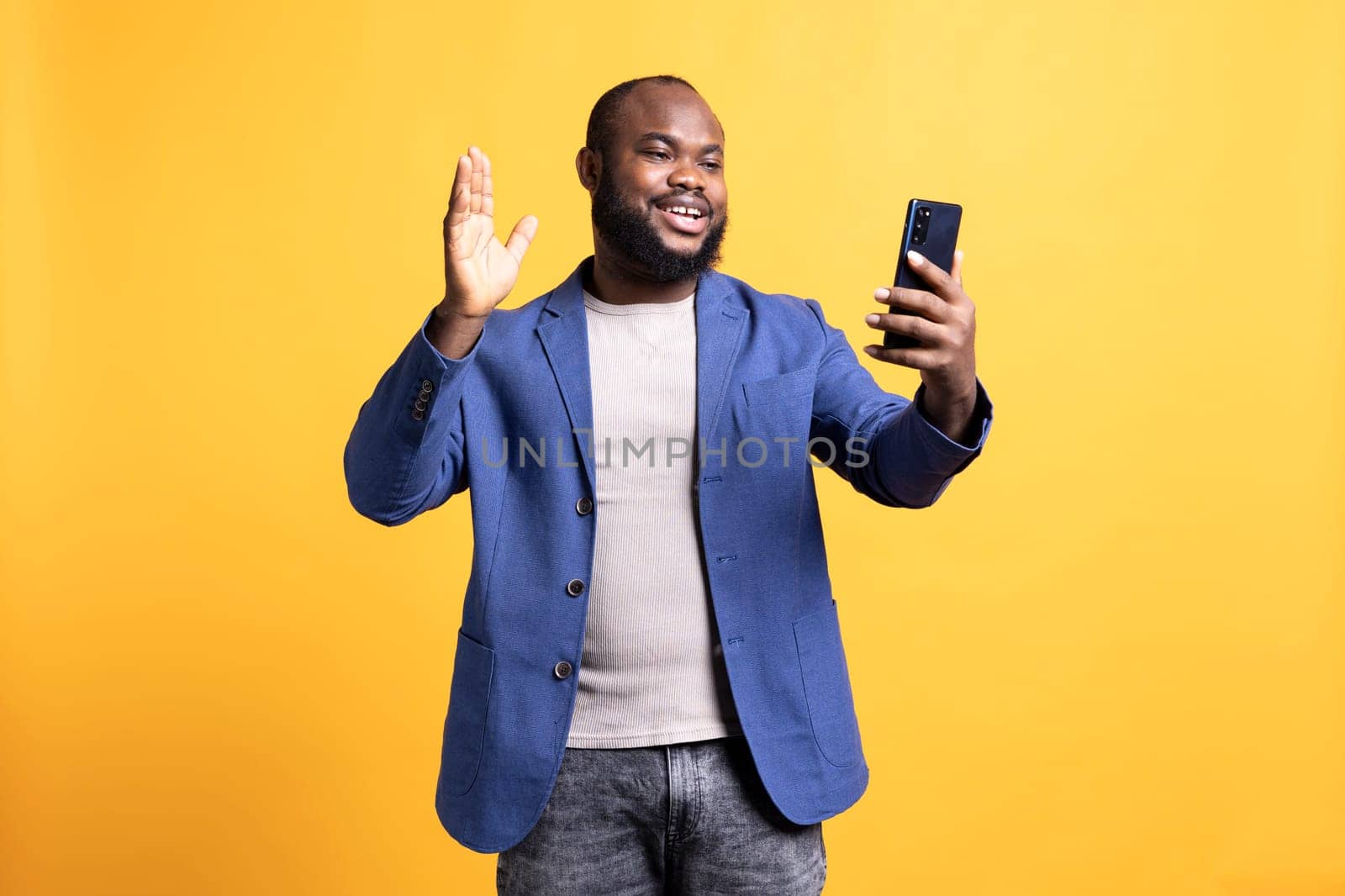 Smiling man having friendly conversation with friends during teleconference meeting using smartphone, studio background. BIPOC person having fun catching up with mates during online videocall