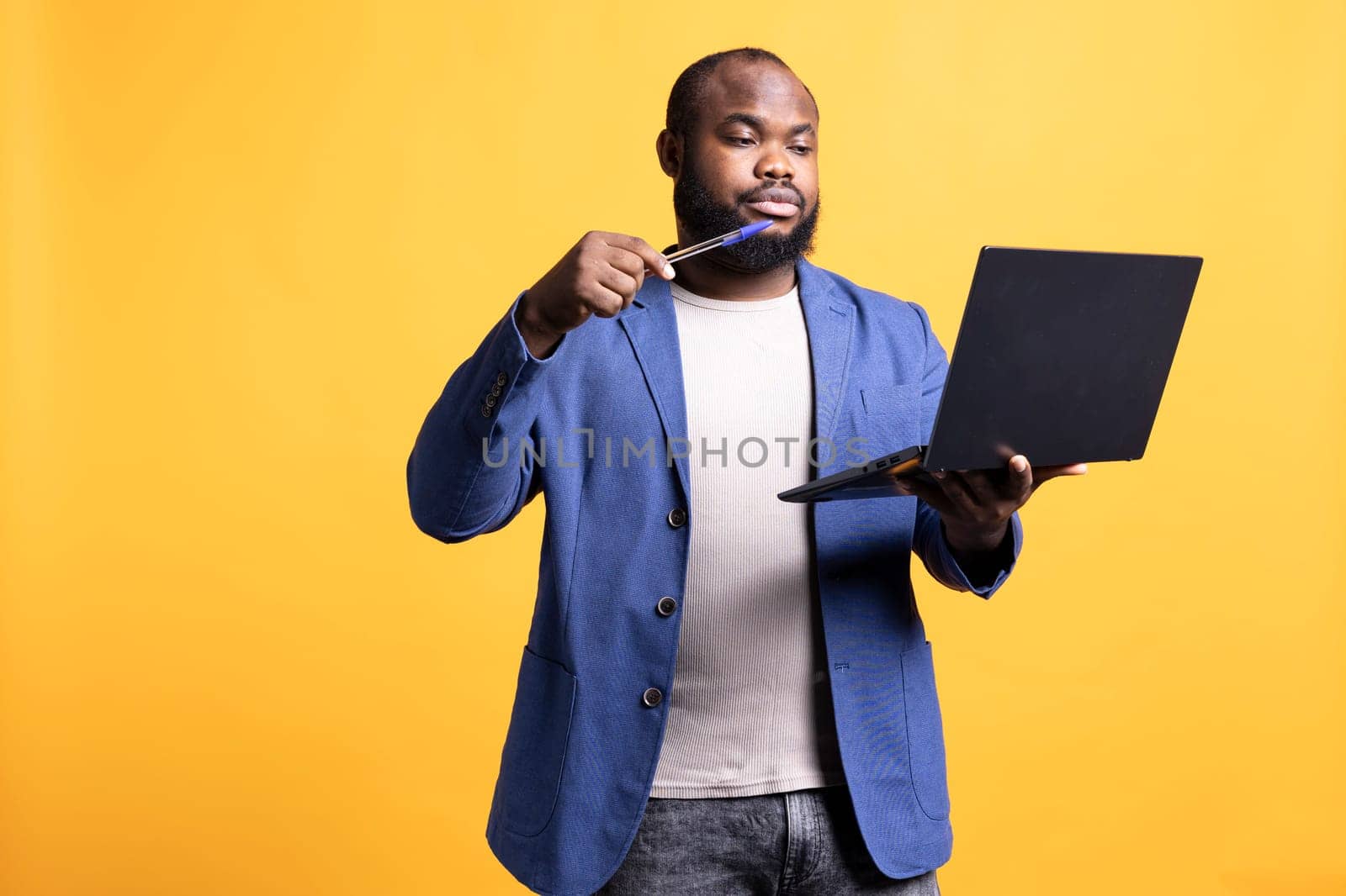 African american man composing email, typing on laptop keyboard, struggling to think of what to write. BIPOC person sending mail online, brainstorming message idea, studio background