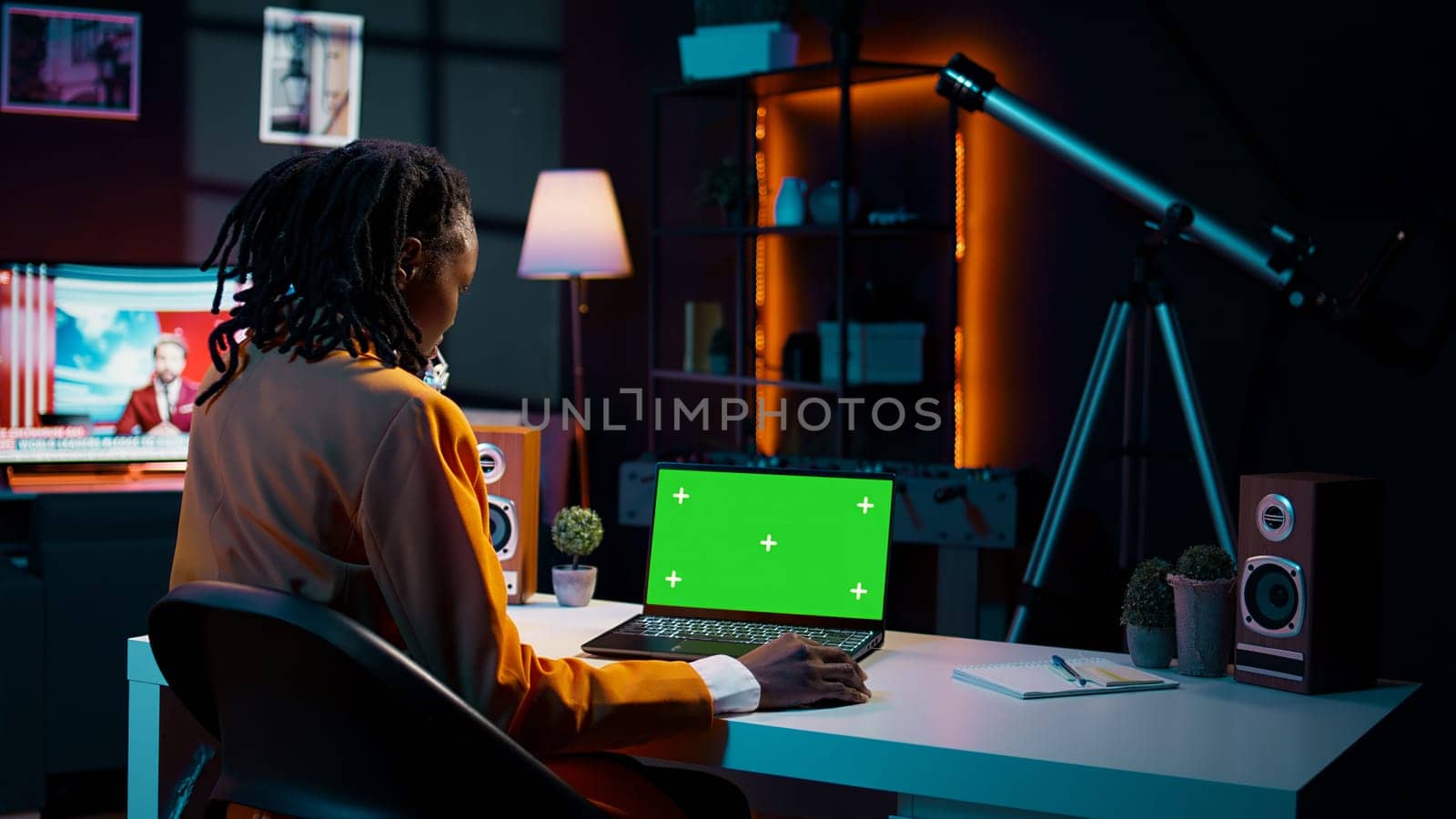 African american young woman looks at laptop with greenscreen, sitting at her home desk and preparing to attend online university lessons. Girl using pc with isolated mockup layout. Camera B.