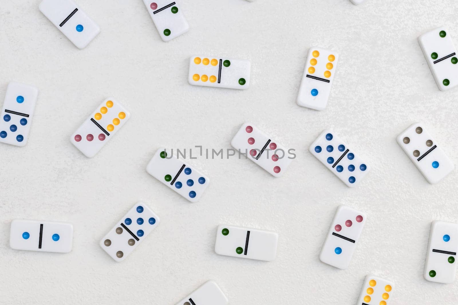 White dominoes with colorful dots lie randomly on a white cement background,flat lay close-up.Concept summer board game.