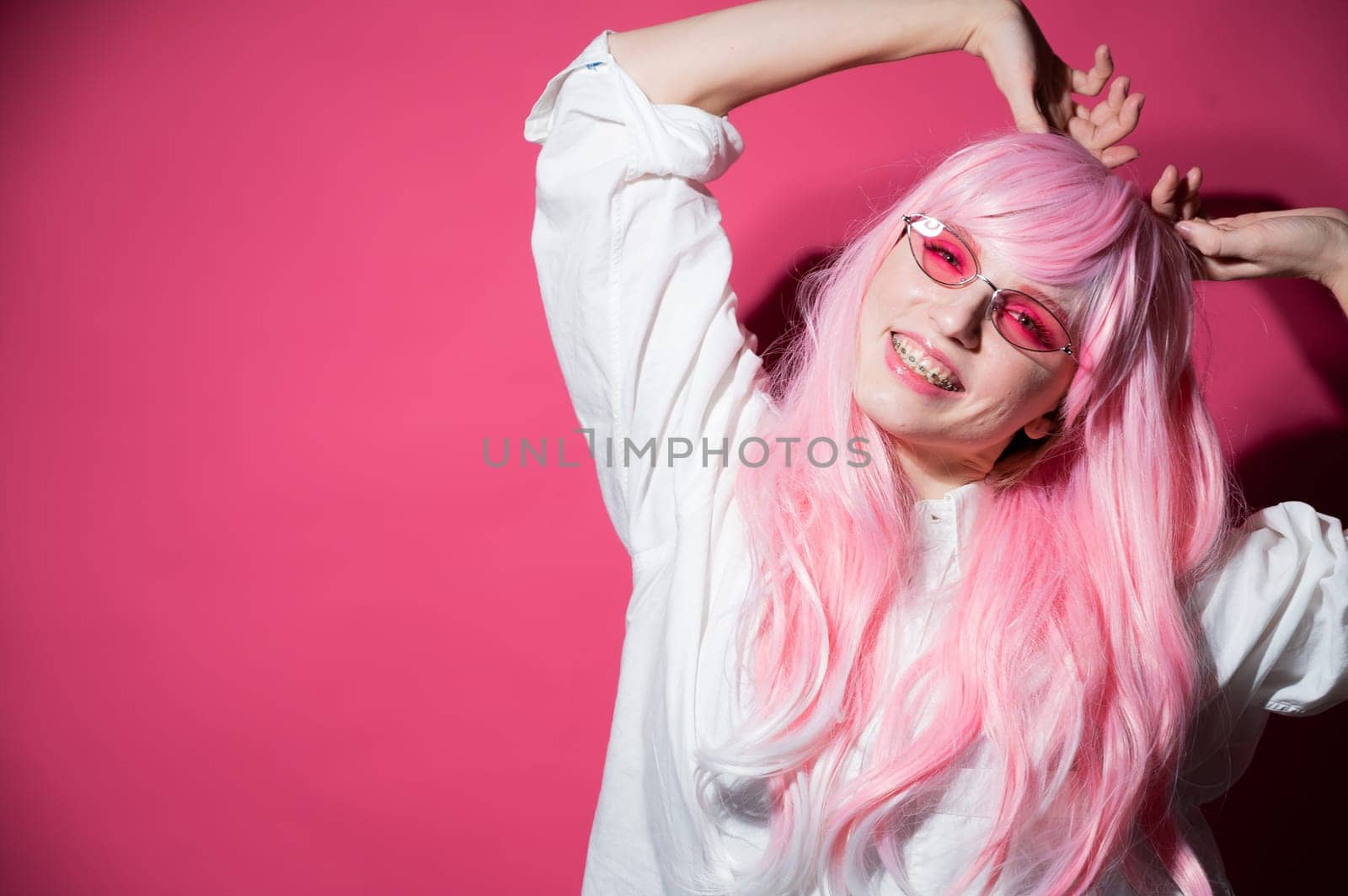 Close-up portrait of a young woman with braces in a pink wig and sunglasses on a pink background. Copy space. by mrwed54
