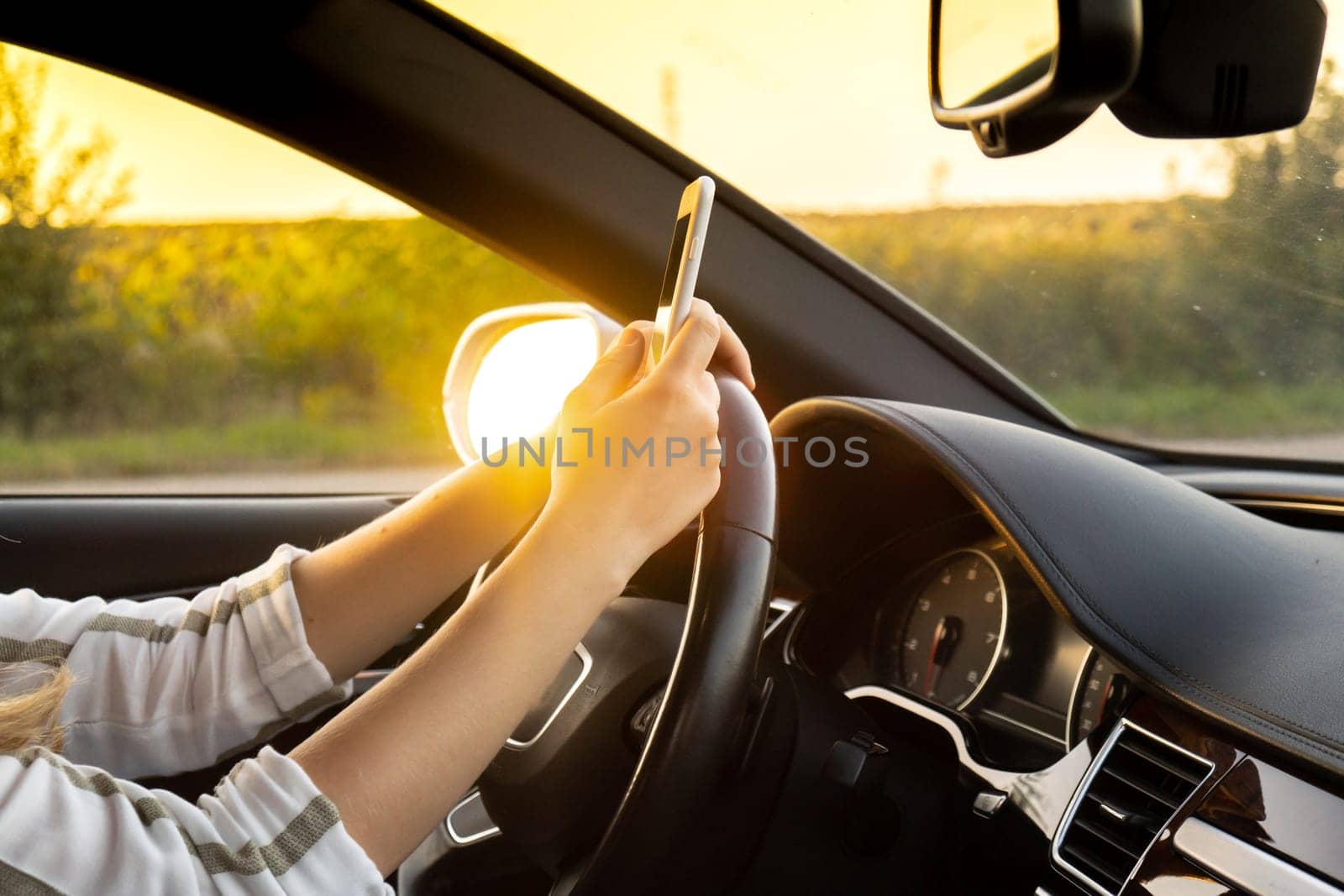 Young woman using mobile phone while driving car on highway road during sunset. Womandriver has accident calling with smartphone for help. Business woman busy driving by anna_stasiia