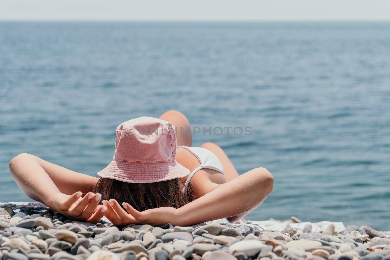 Unrecognizable positive woman in white bikini sunbathing or tanning on seaside beach during summer. happy tourist enjoying sun tan lying on beach chair lounge at luxury resort by panophotograph