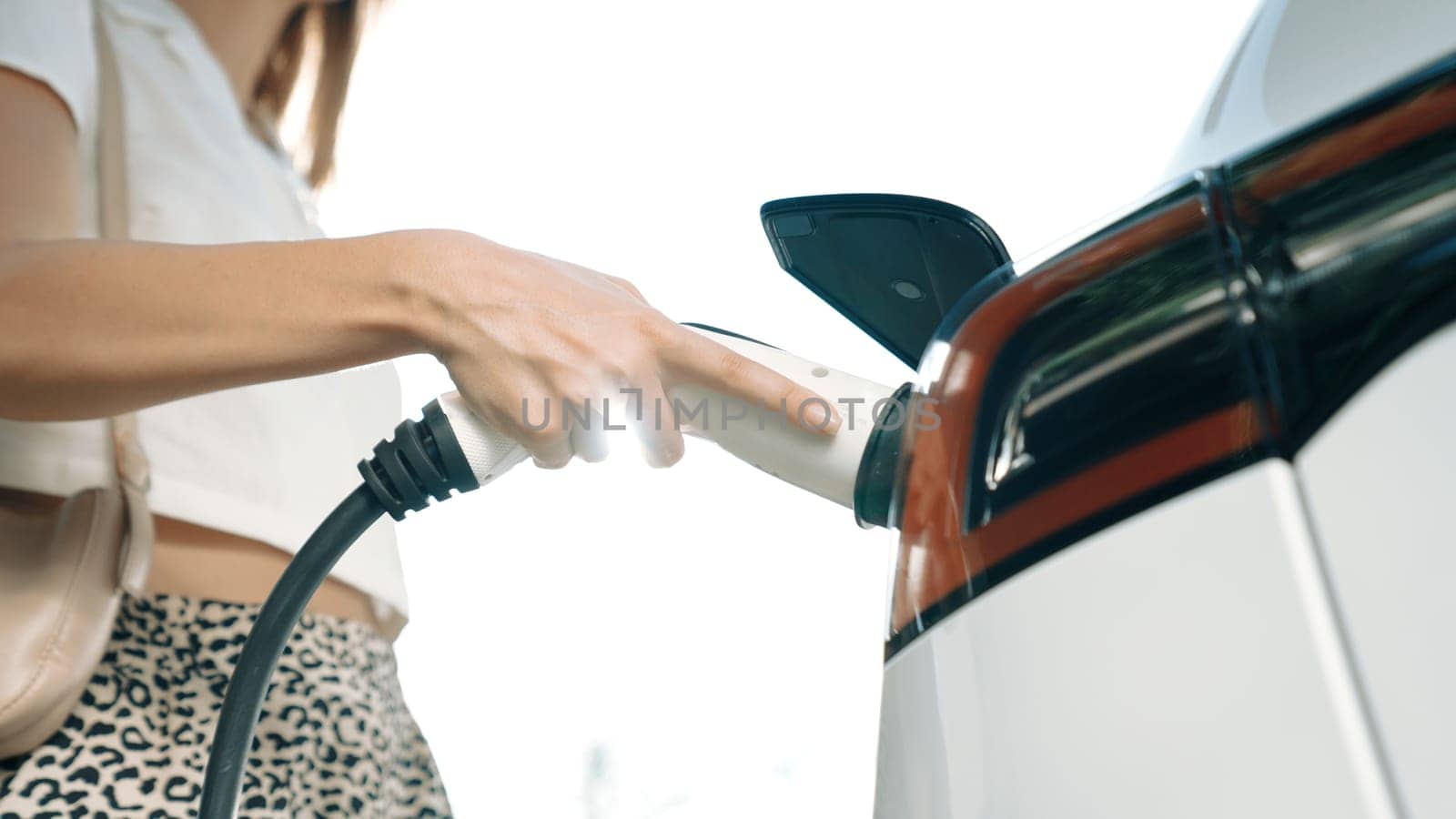 Sunlight backlit brighten young woman travel with EV electric car charging in green sustainable city outdoor garden in summer. Green urban sustainability lifestyle by electric vehicle innards