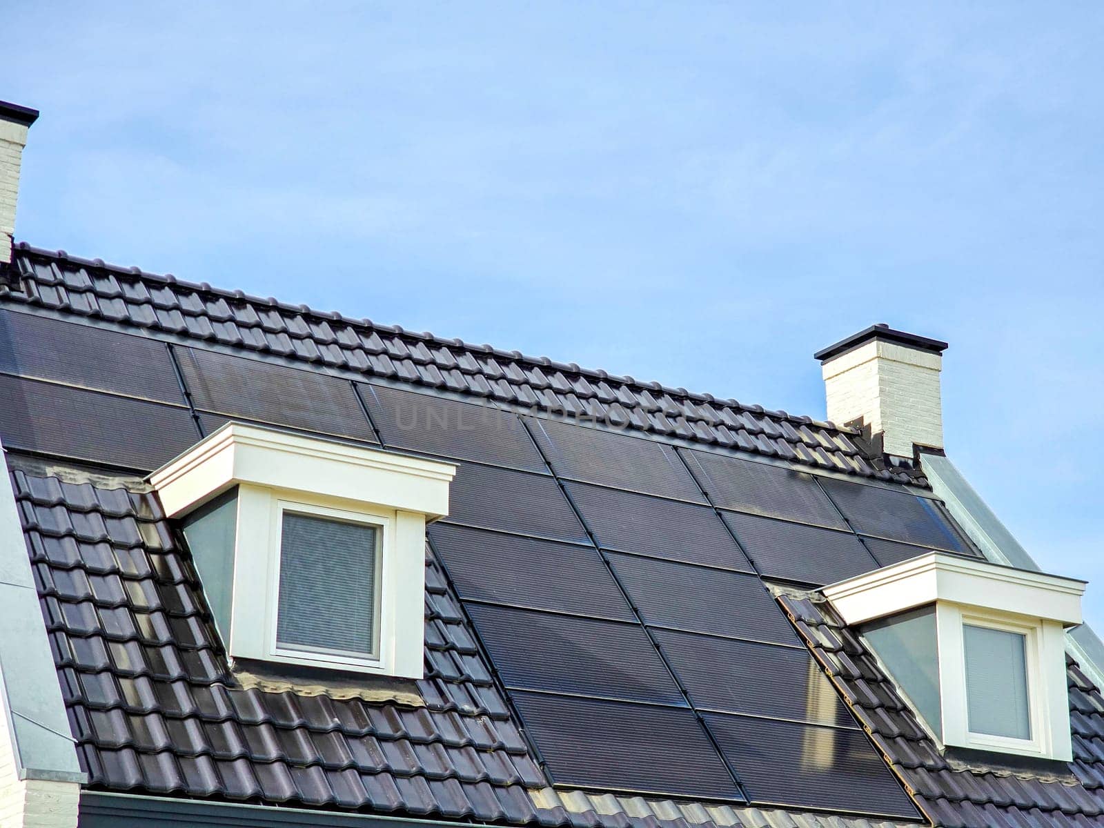 house with black solar panels on the roof against a sunny sky Close up of new building with black solar panels. Zonnepanelen, Zonne energie, Translation: Solar panel, Sun Energy, energy transition