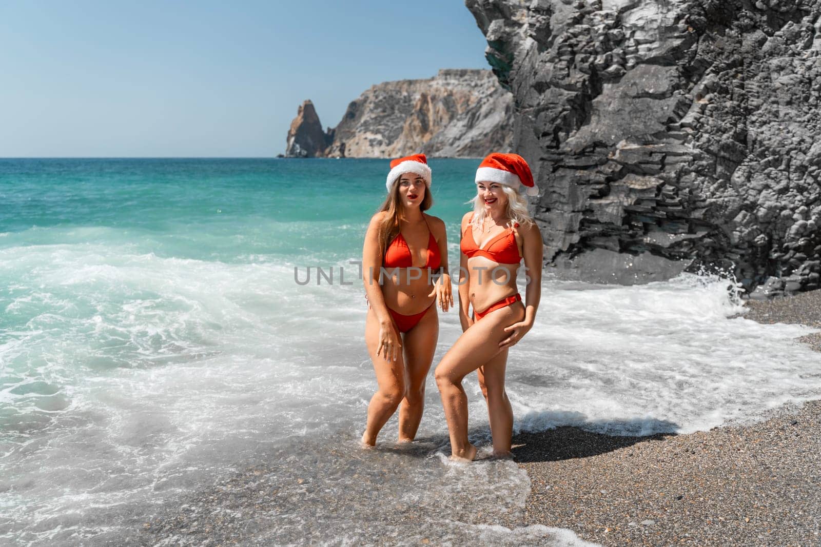 Women in Santa Claus hats run into the sea dressed in red swimsuits. Celebrating the New Year in a hot country by Matiunina