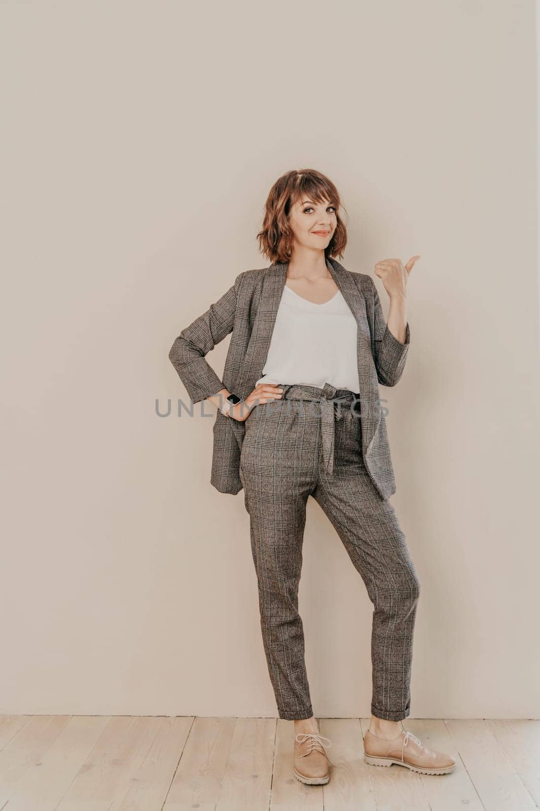Brunette suit wall. Business woman in a beige suit posing on a beige background. Full length studio portrait. by Matiunina