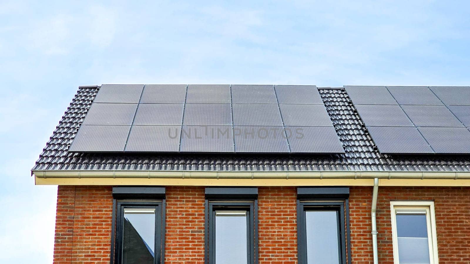 New house with black solar panels on the roof against a sunny sky Close up of new building with black solar panels. Zonnepanelen, Zonne energie, Translation: Solar panel, Sun Energy