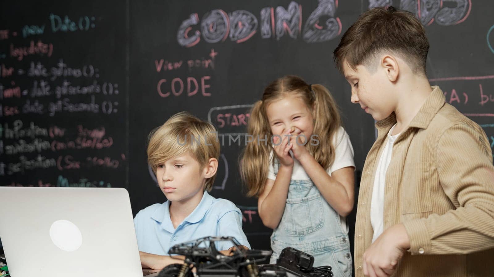 Closeup of boy using laptop programing engineering code and writing program while group of smart diverse student standing surrounded by friend in STEM technology classroom at blackboard. Erudition.