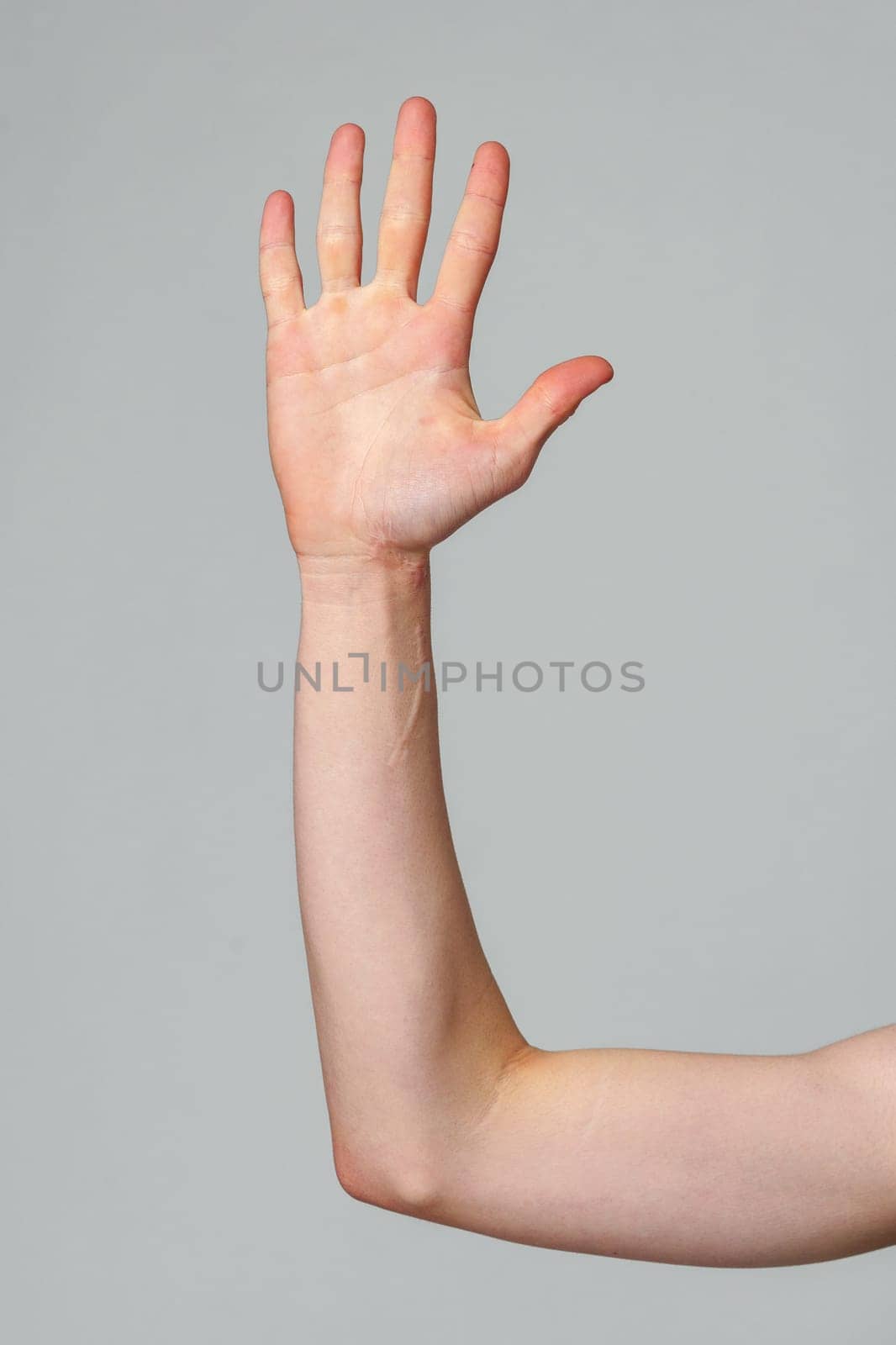 A person standing with one hand raised high in the air, reaching towards the sky. The individuals palm is open and fingers are extended, showcasing a gesture of strength or readiness.