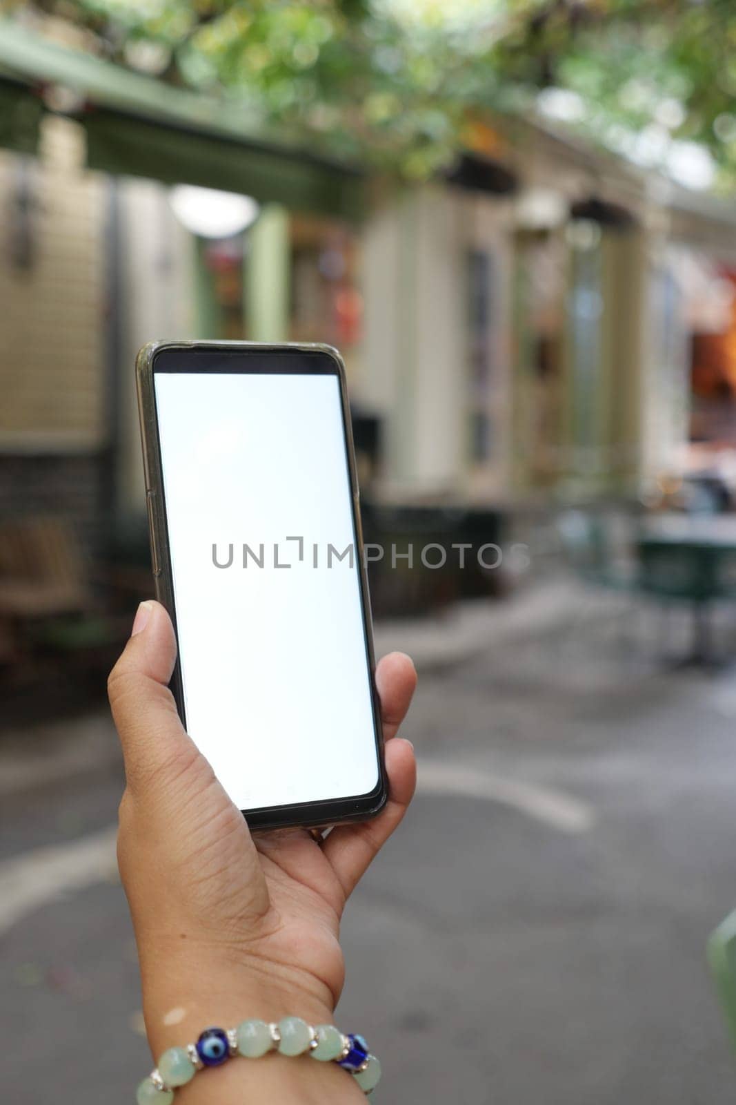 holding smart phone with empty screen with blurred cafe street background. by towfiq007