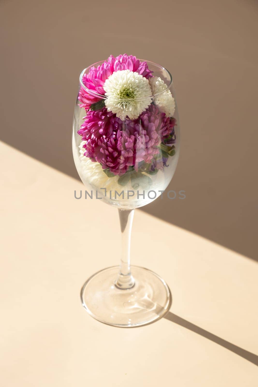 Wine glass full of colorful flowers. Creative concept for holidays greeting card postcard. Minimalistic isometric style. Drinking beauty bouquet. Copy space
