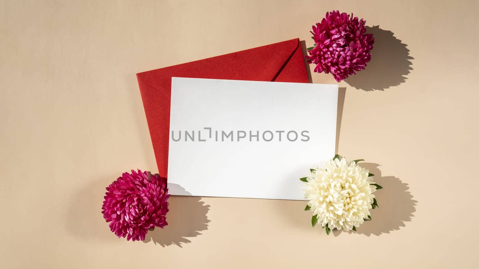 Beautiful little white flowers on postal red envelope on beige background, empty paper note copy space for text, spring time, greeting card for holiday. Flower delivery concept