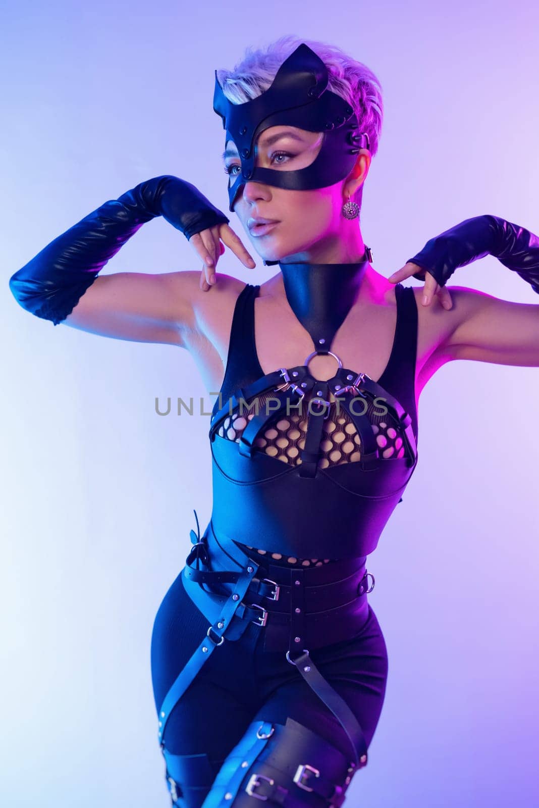 A sexy girl in the erotic image of a catwoman in leather bdsm straps and a mask poses against a copy paste background on a beautiful neon background by Rotozey