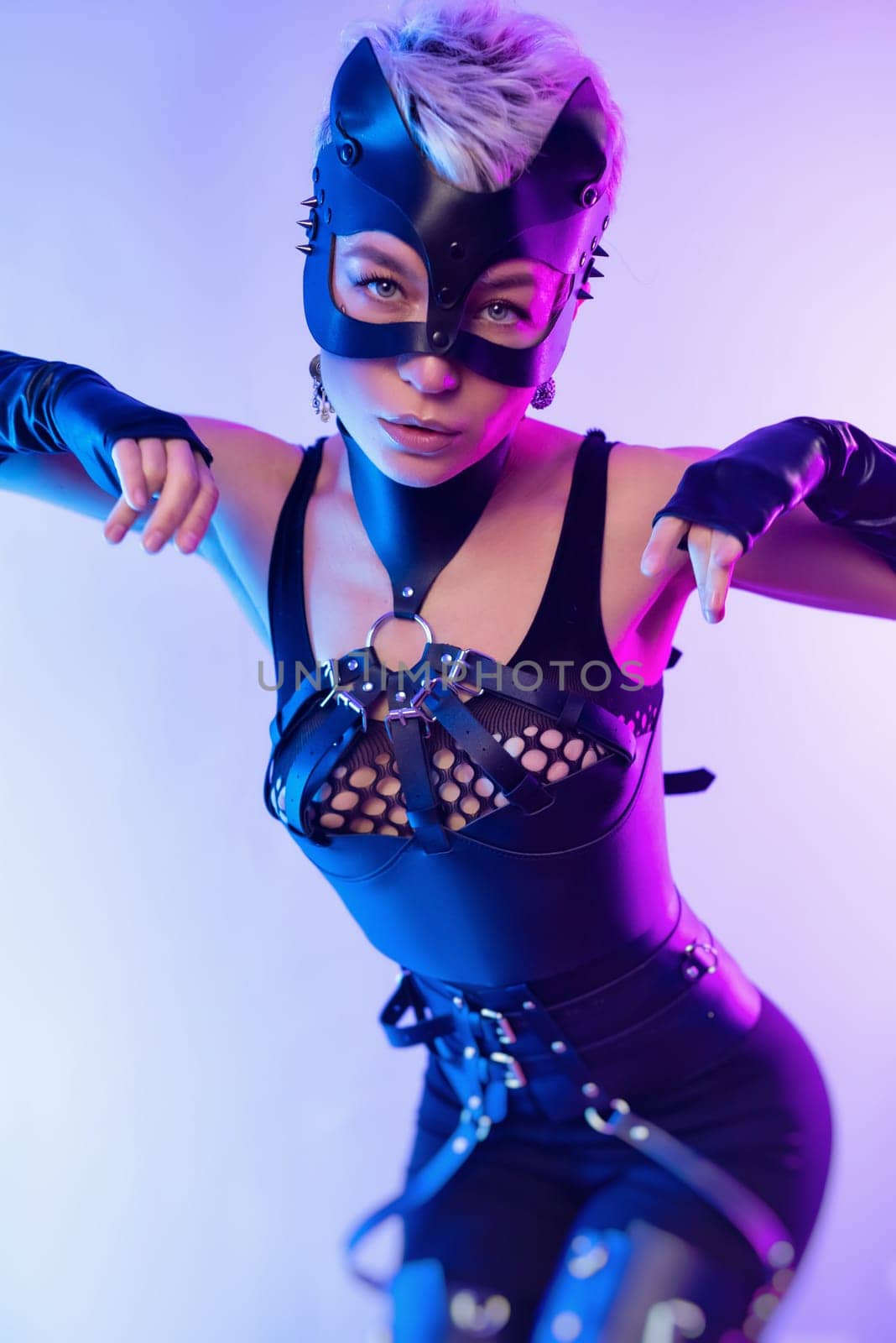 A sexy girl in the erotic image of a catwoman in leather bdsm straps and a mask poses against a copy paste background on a beautiful neon background by Rotozey