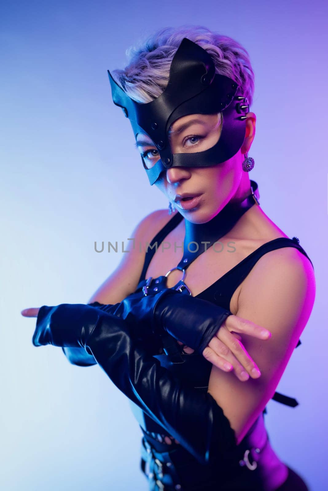 A sexy girl in the erotic image of a catwoman in leather bdsm straps and a mask poses against a copy paste background on a beautiful neon background by Rotozey