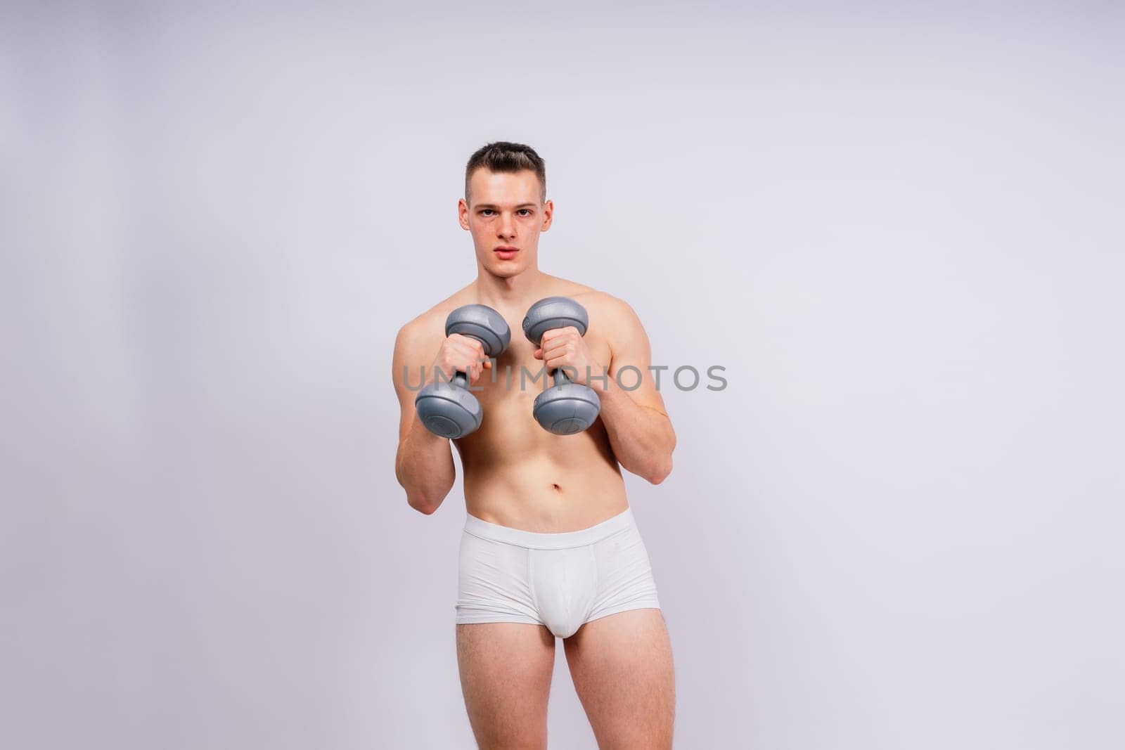 Man with pumped-up body with dumbbells in his hands white panties exercise