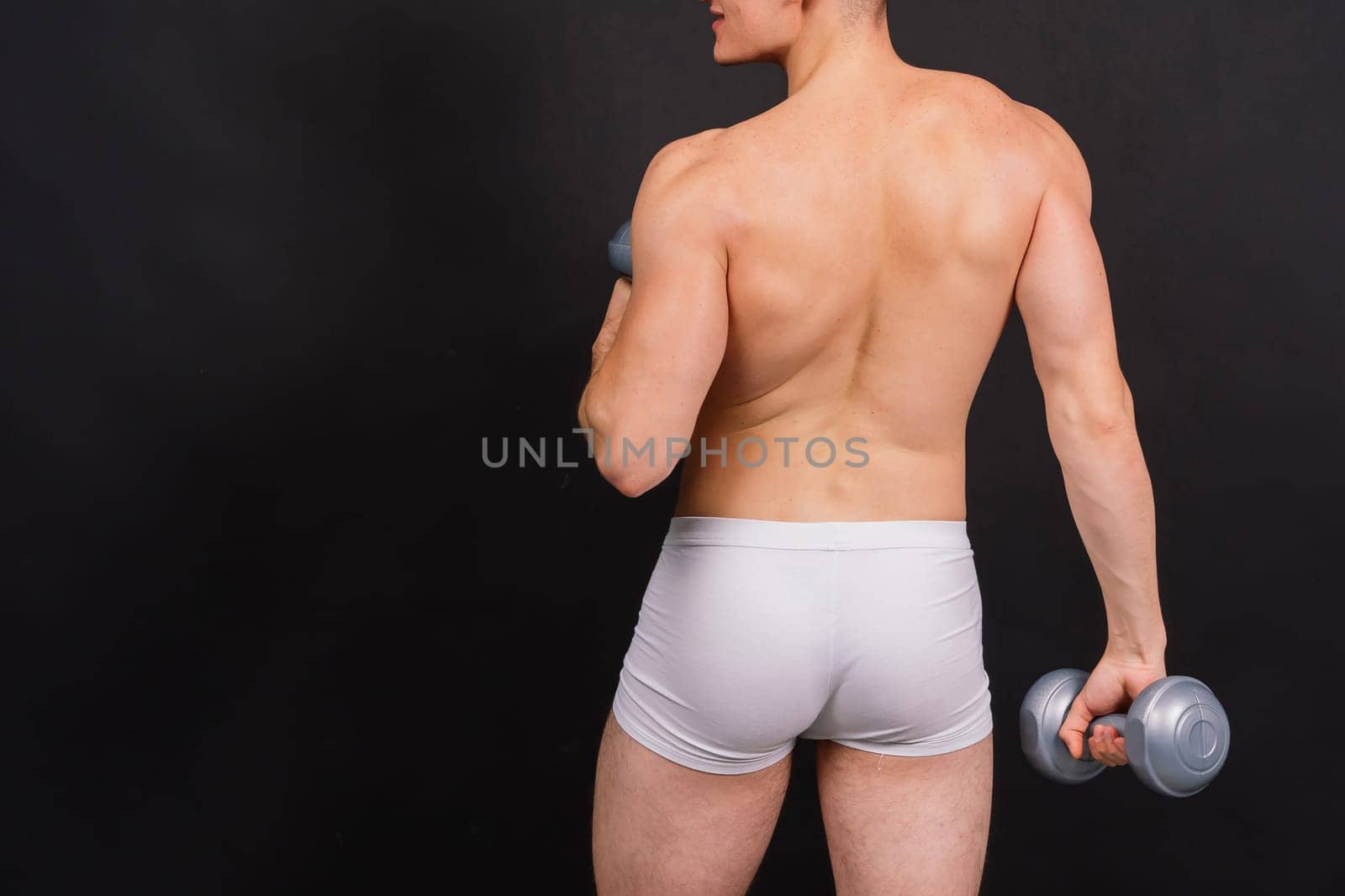 Man with pumped-up body with dumbbells in his hands white panties exercise