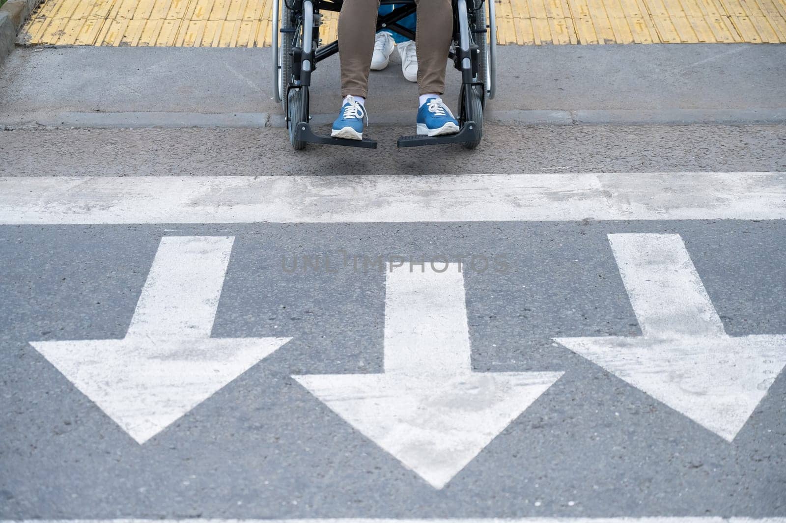 An elderly woman in a wheelchair is about to cross the road at a pedestrian crossing. by mrwed54