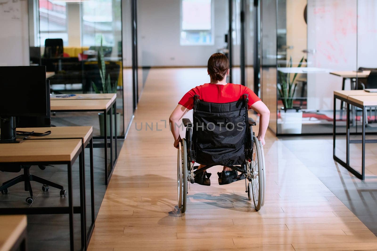 A modern young businesswoman in a wheelchair is surrounded by an inclusive workspace with glass-walled offices, embodying determination and innovation in the business world by dotshock