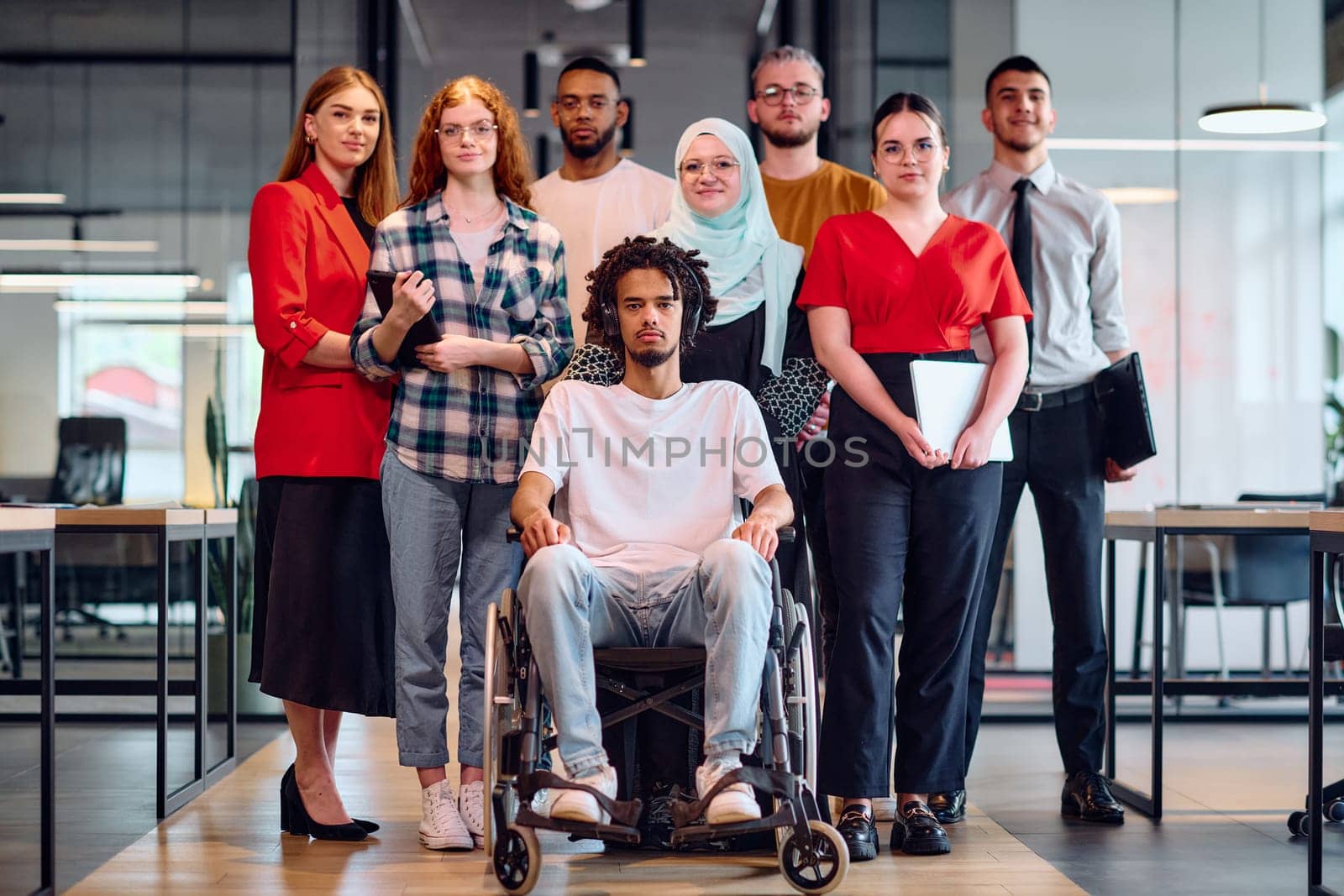 A diverse group of young business people walking a corridor in the glass-enclosed office of a modern startup, including a person in a wheelchair and a woman wearing a hijab by dotshock