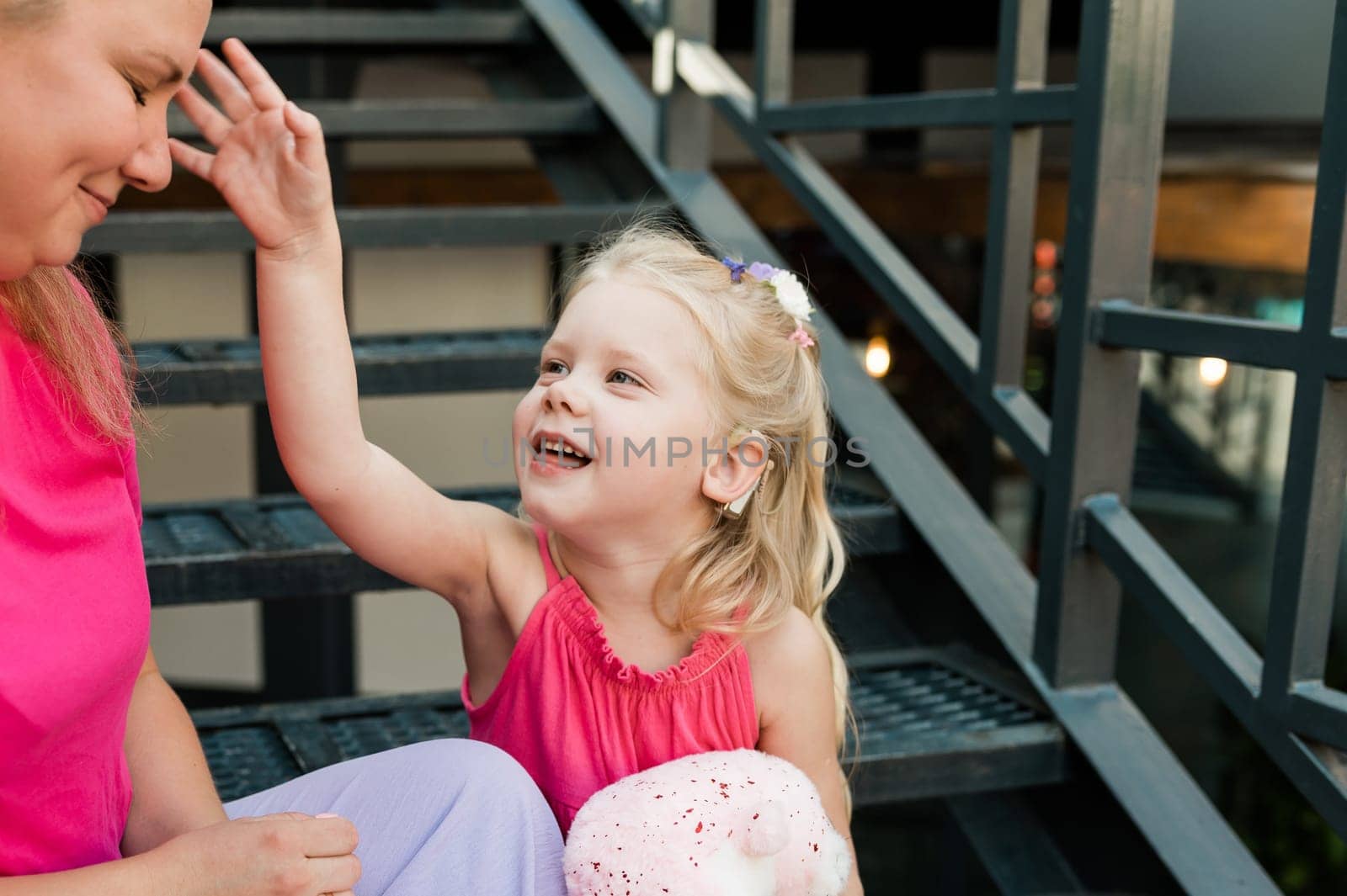 Deaf child with cochlear implant for hearing audio and aid for impairment having fun and laughs with mother outdoor in summer. Sound fitting device to help with communication listening and interaction.