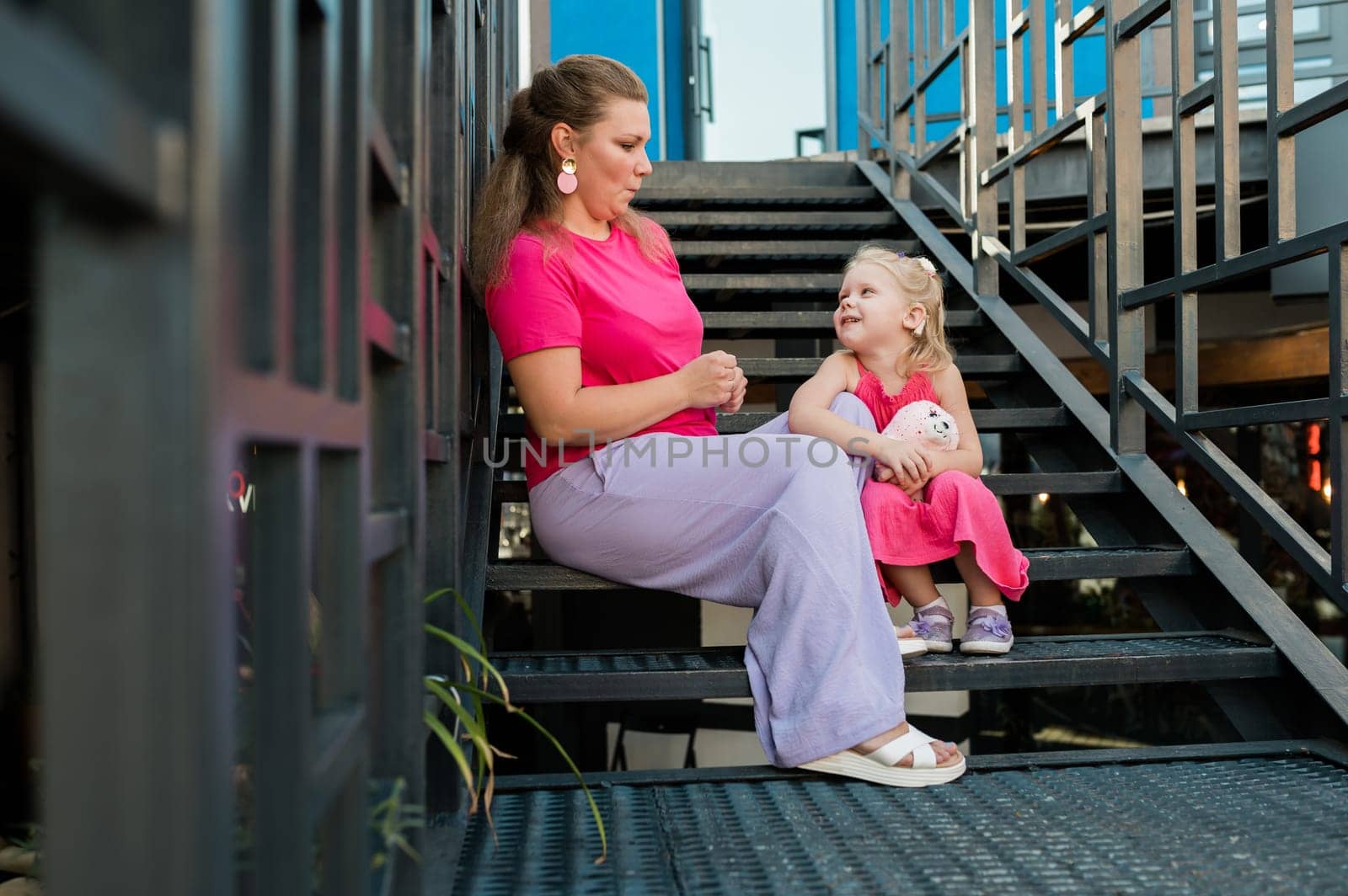 Deaf child with cochlear implant for hearing audio and aid for impairment having fun and laughs with mother outdoor in summer. Sound fitting device to help with communication listening and interaction.