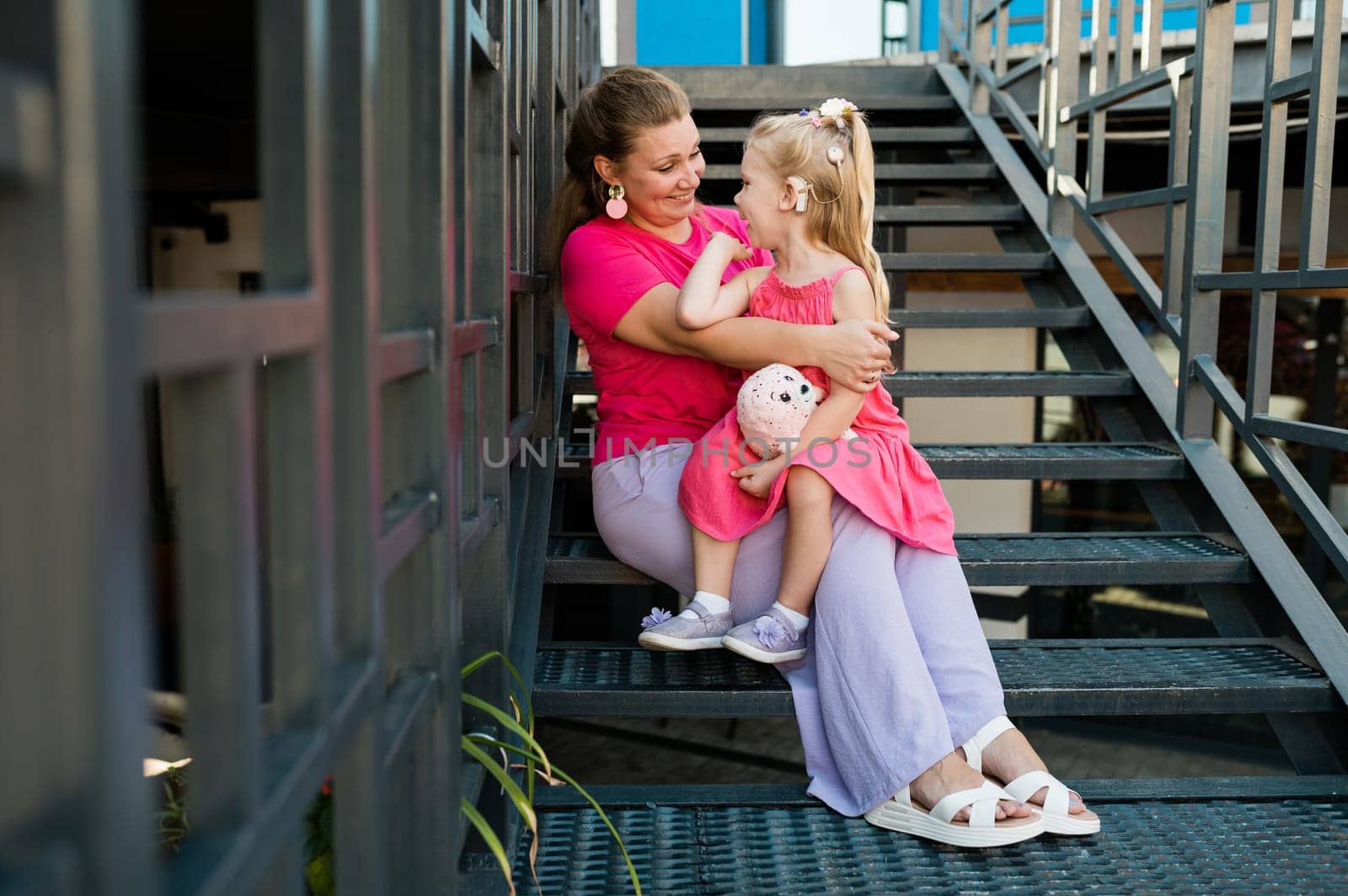 Mother holds and have fun her child with hearing aids and cochlear implants summer outdoor . Deaf and health concept. Diversity and inclusion. Copy space.