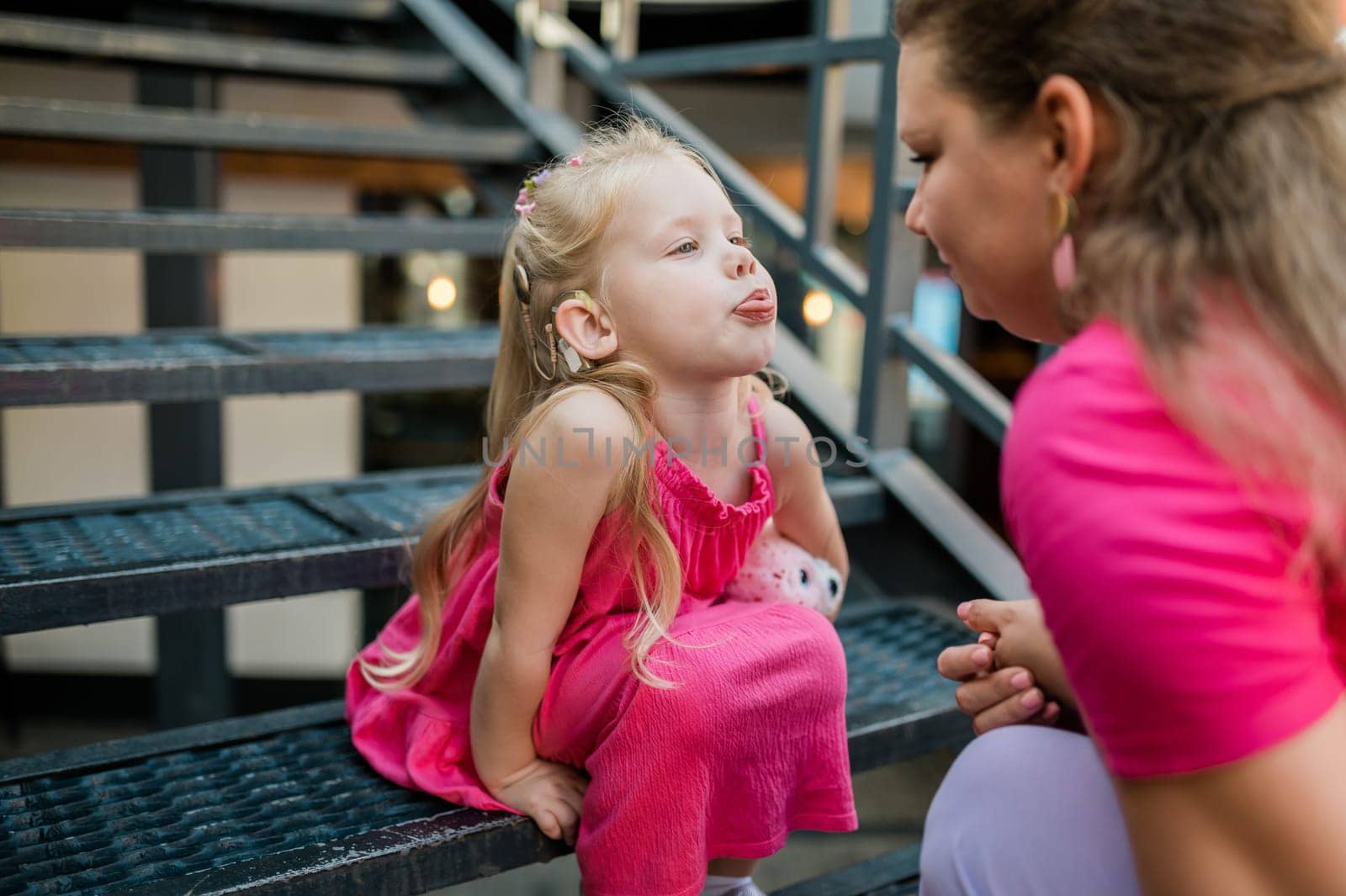 Mother holds and have fun her child with hearing aids and cochlear implants summer outdoor . Deaf and health concept. Diversity and inclusion. Copy space.