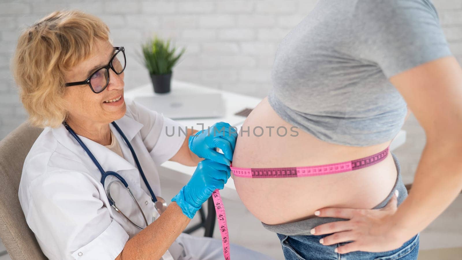 Doctor measuring the volume of a pregnant woman's abdomen using a centimeter tape