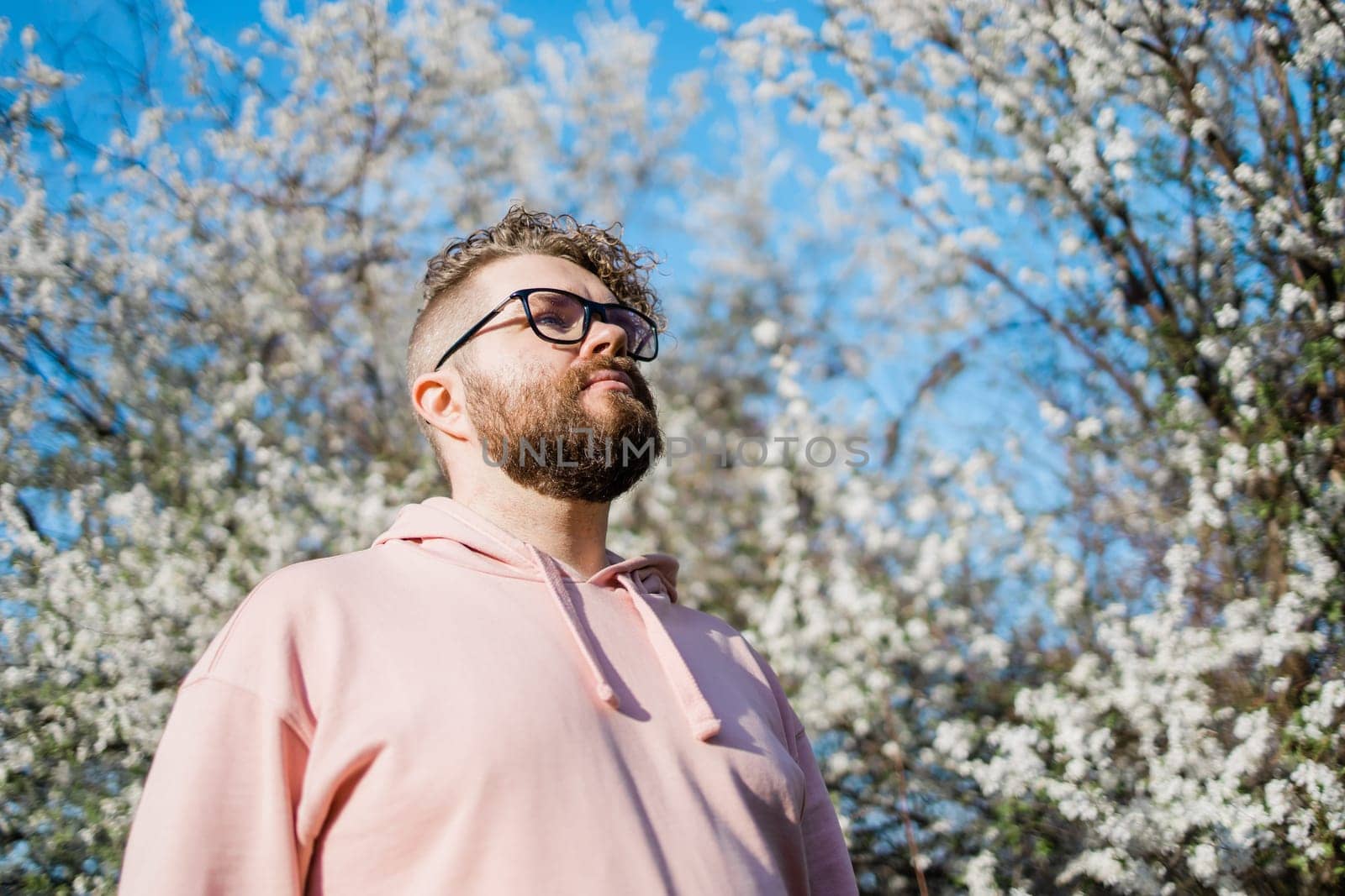 Handsome man outdoors portrait on background cherry blossoms or apple blossoms and blue spring sky. Millennial generation guy and new masculinity concept by Satura86