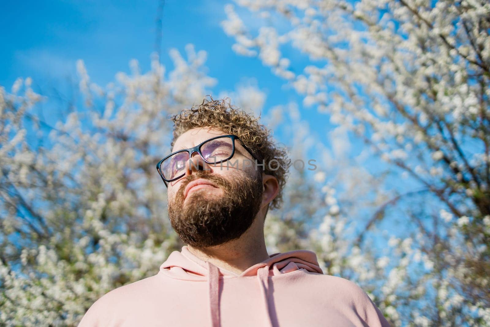 Handsome man outdoors portrait on background cherry blossoms or apple blossoms and blue spring sky. Millennial generation guy and new masculinity