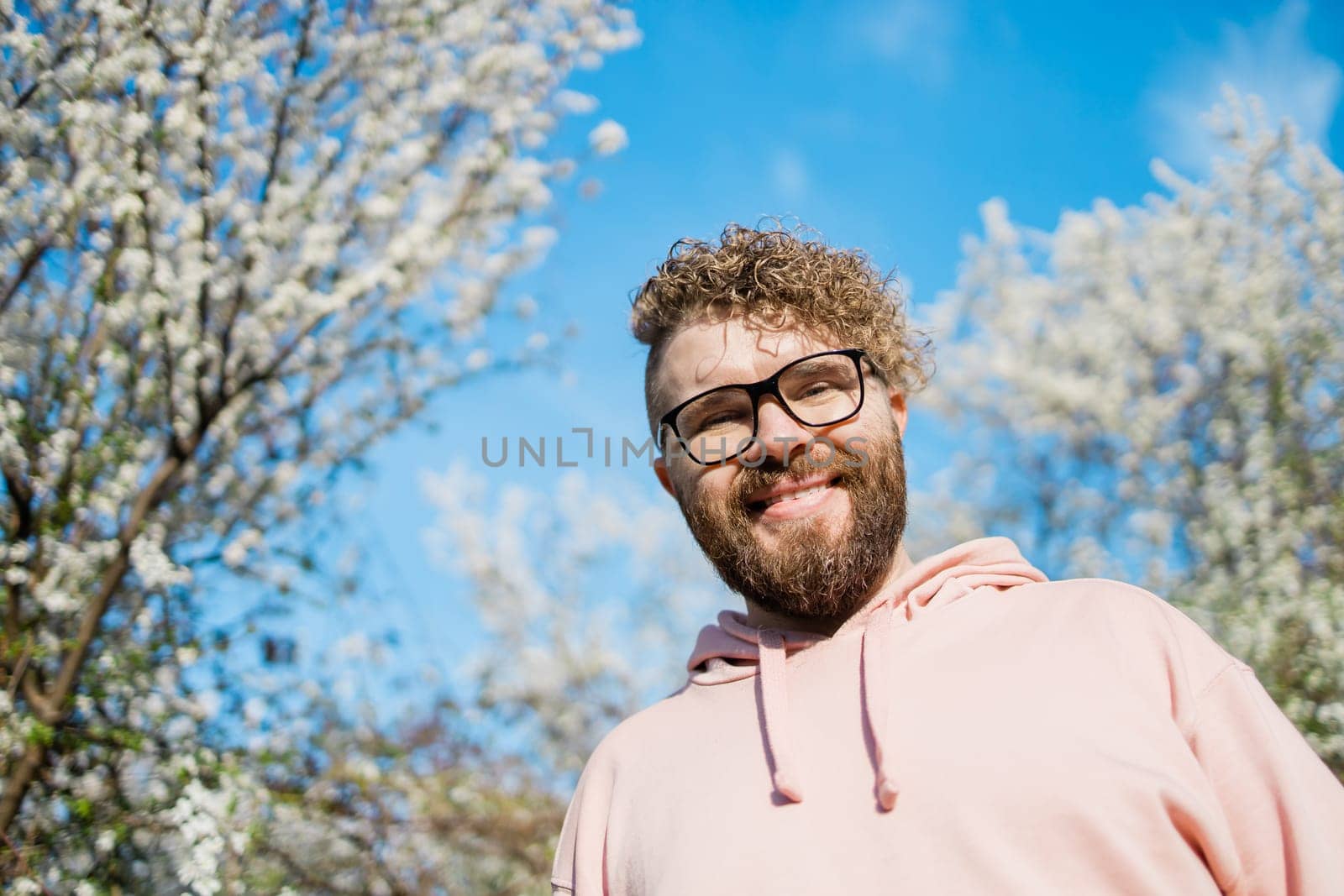 Handsome man outdoors portrait on background cherry blossoms or apple blossoms and blue spring sky. Millennial generation guy and new masculinity concept by Satura86