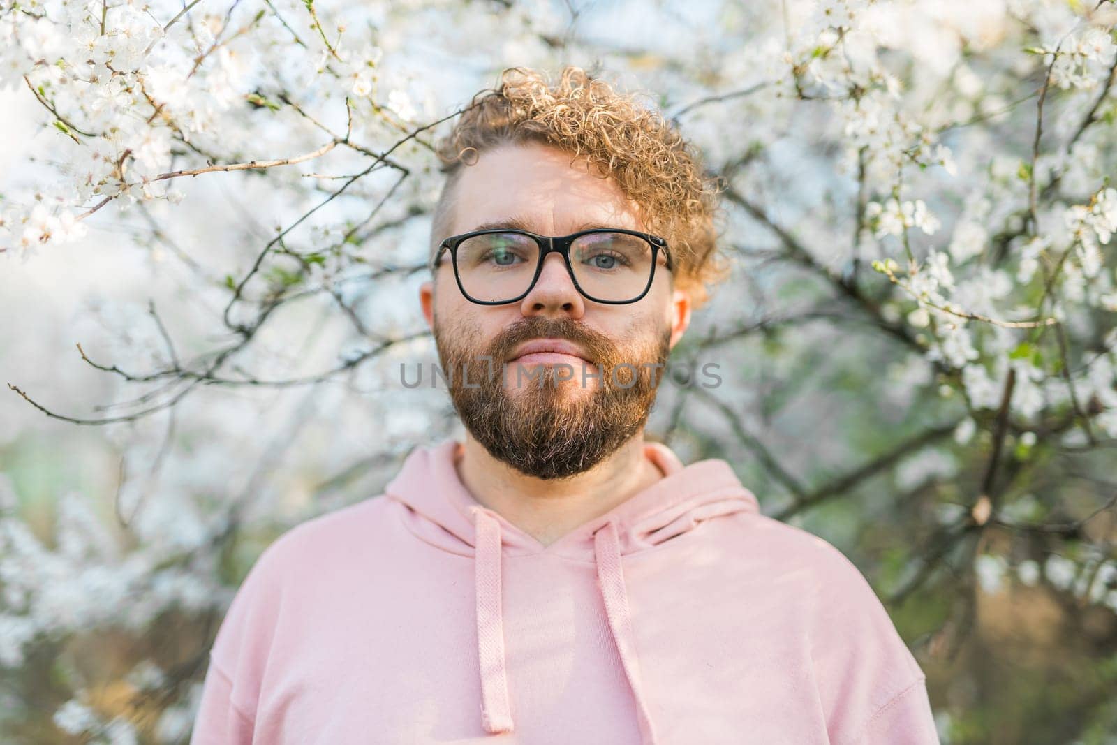 Handsome man outdoors portrait on background cherry blossoms or apple blossoms and blue spring sky. Millennial generation guy and new masculinity