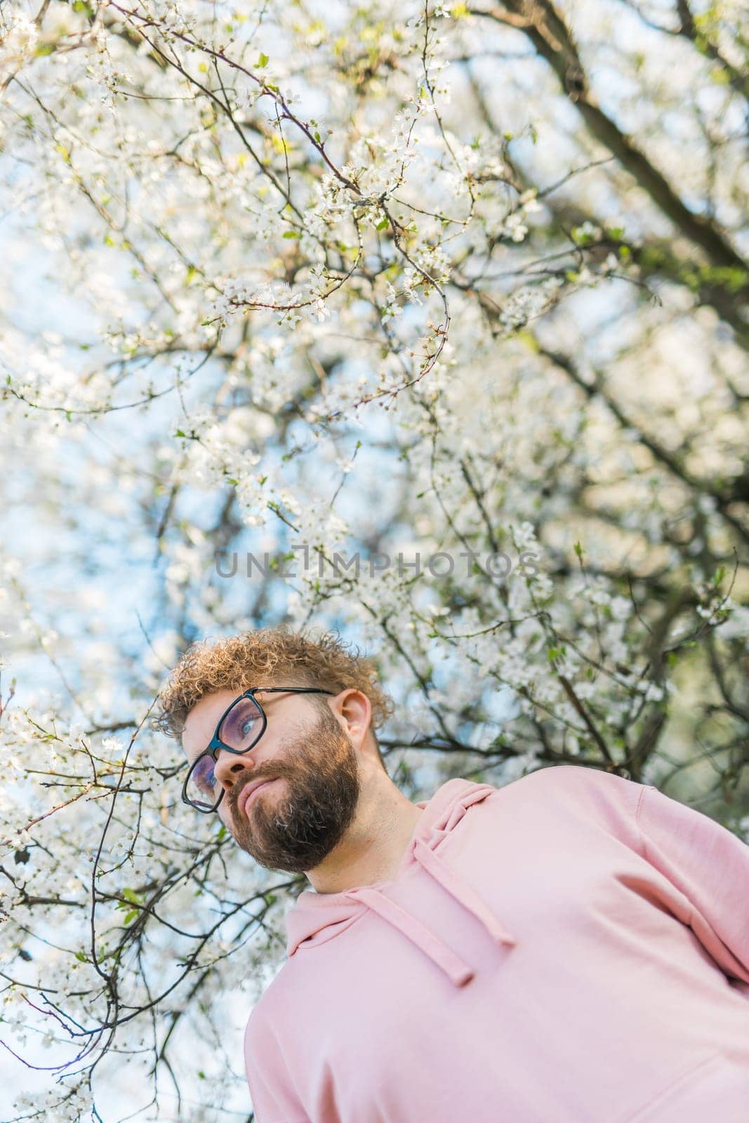 Handsome man outdoors portrait on background cherry blossoms or apple blossoms. Millennial generation guy and new masculinity concept by Satura86