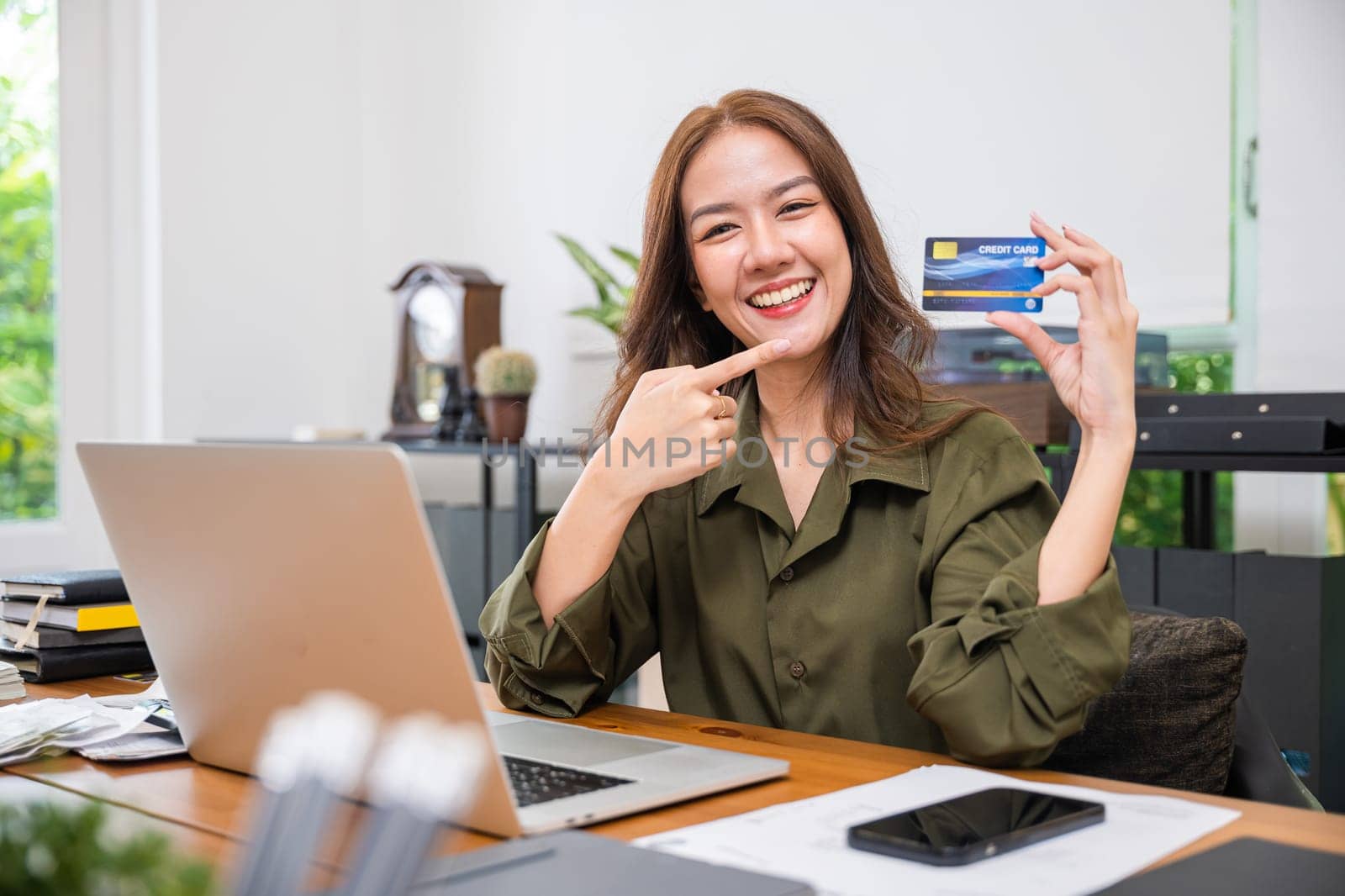 woman excited holding credit card and pointing the card with laptop computer by Sorapop