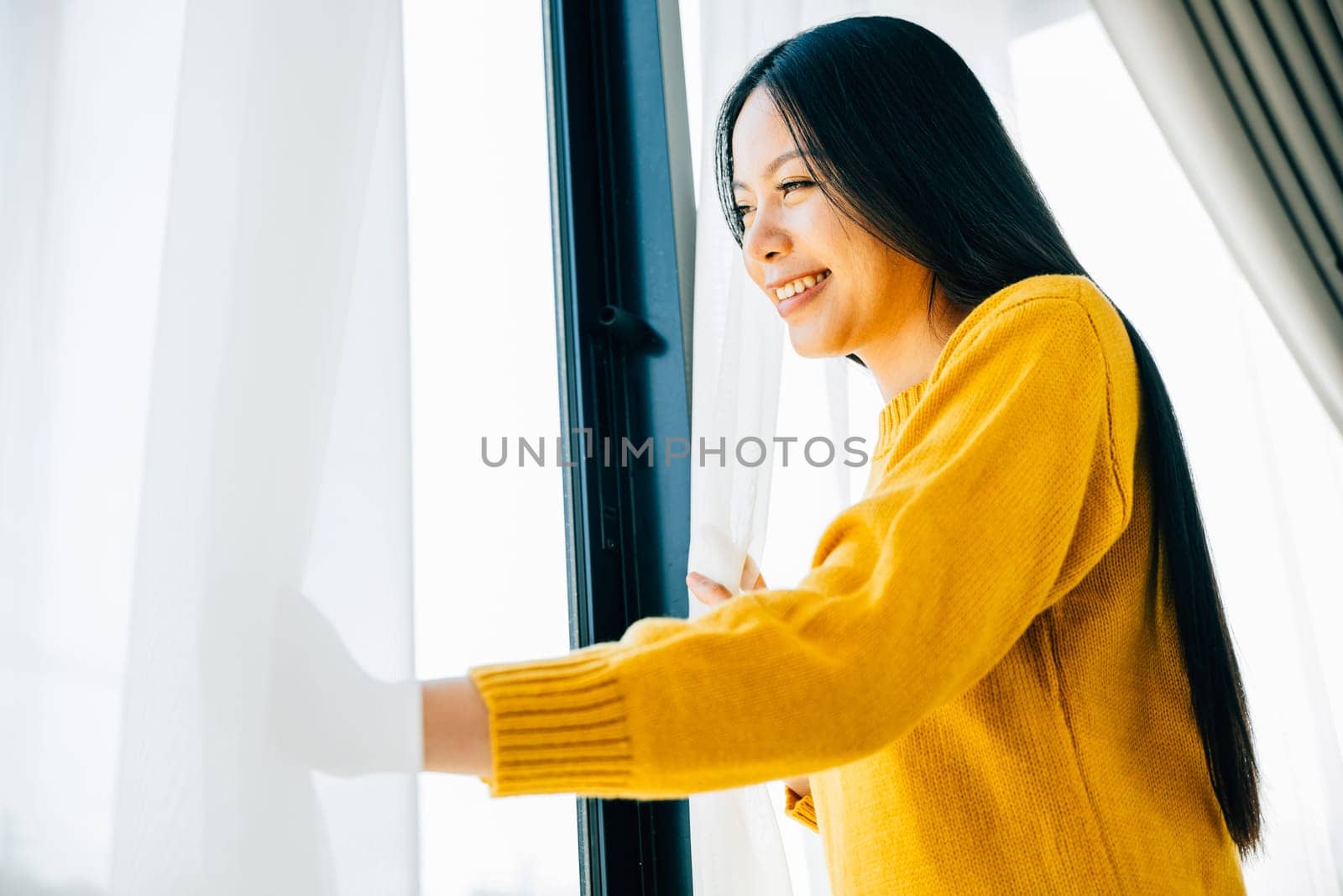 A young woman opens curtains smiles at the view feeling refreshed and joyful at home. Reflecting morning happiness relaxation and a cheerful beginning.