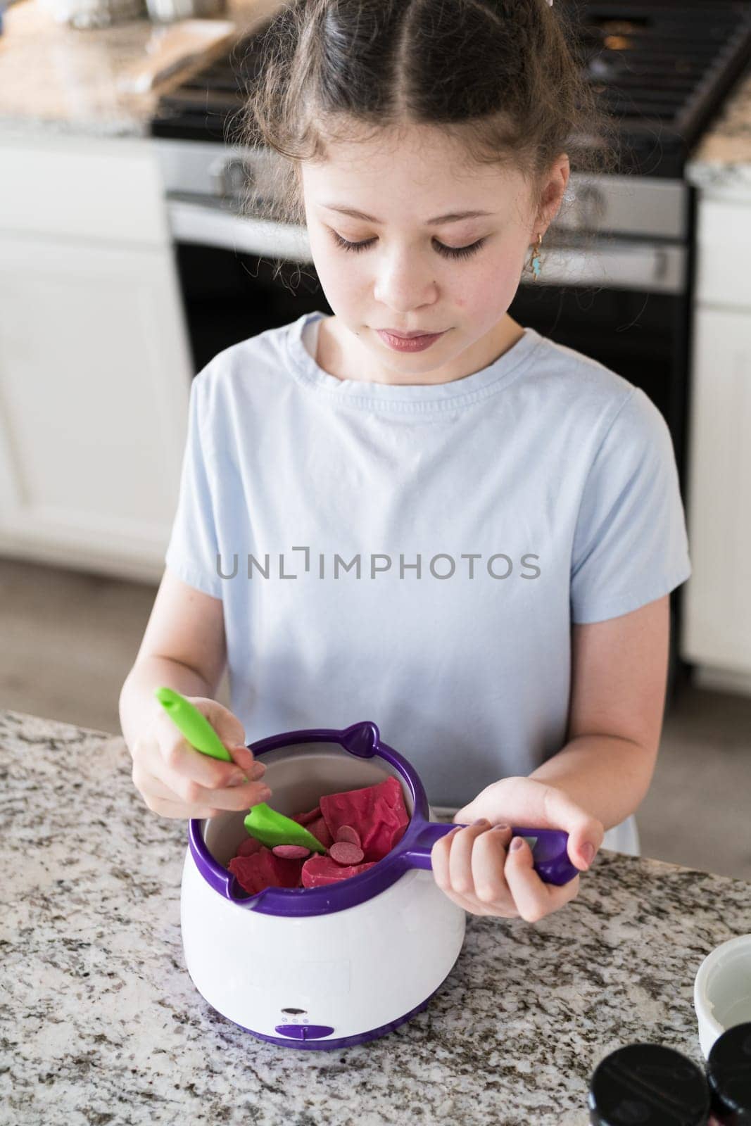 With focused attention, this budding culinary artist dips pretzels into a pot of melted chocolate, creating sweet delights in the warmth of a well-lit home kitchen.