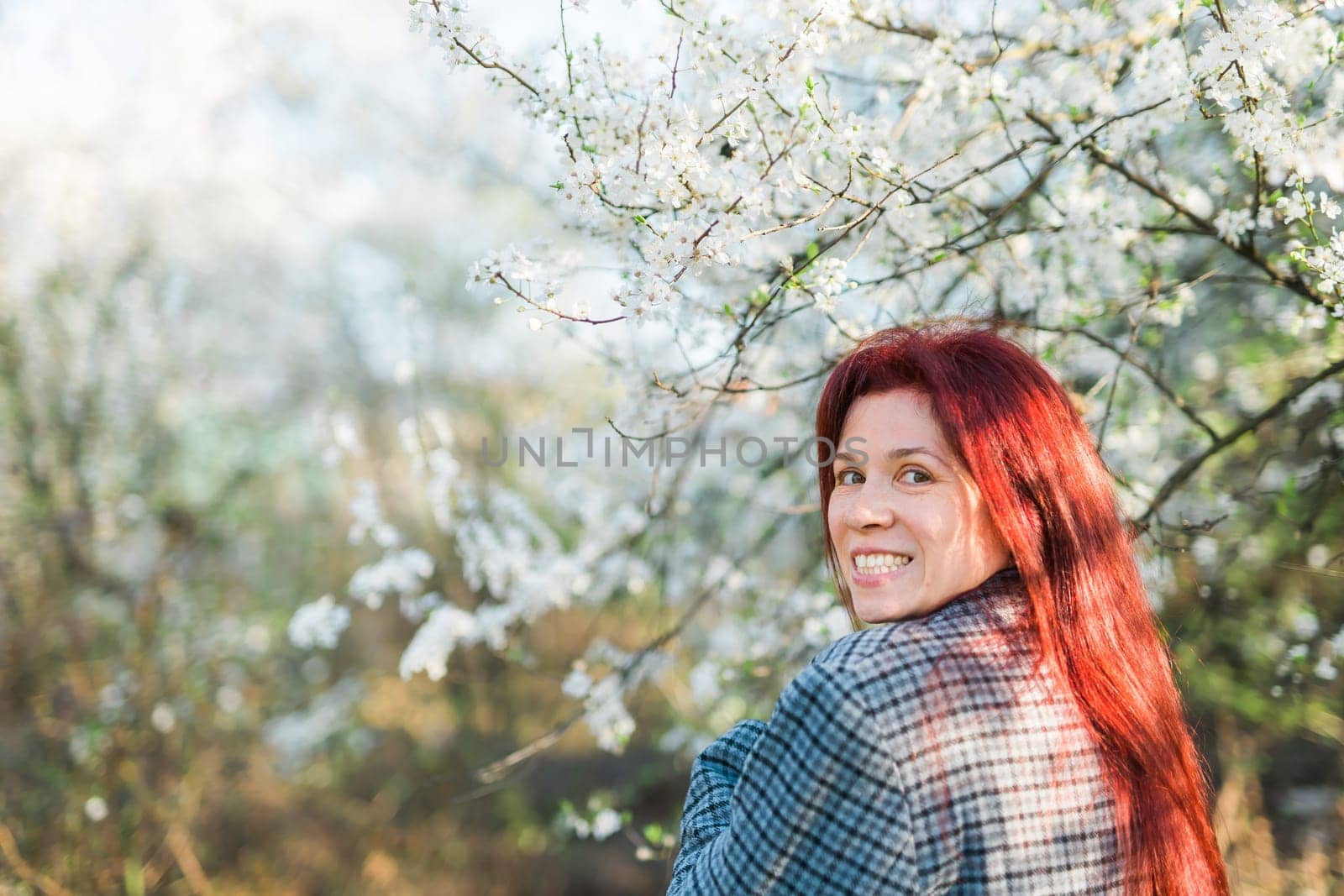 Beautiful happy millennial woman enjoying smell in a flowering spring garden. Blooming tree time. Copy space and empty place for advertising text by Satura86