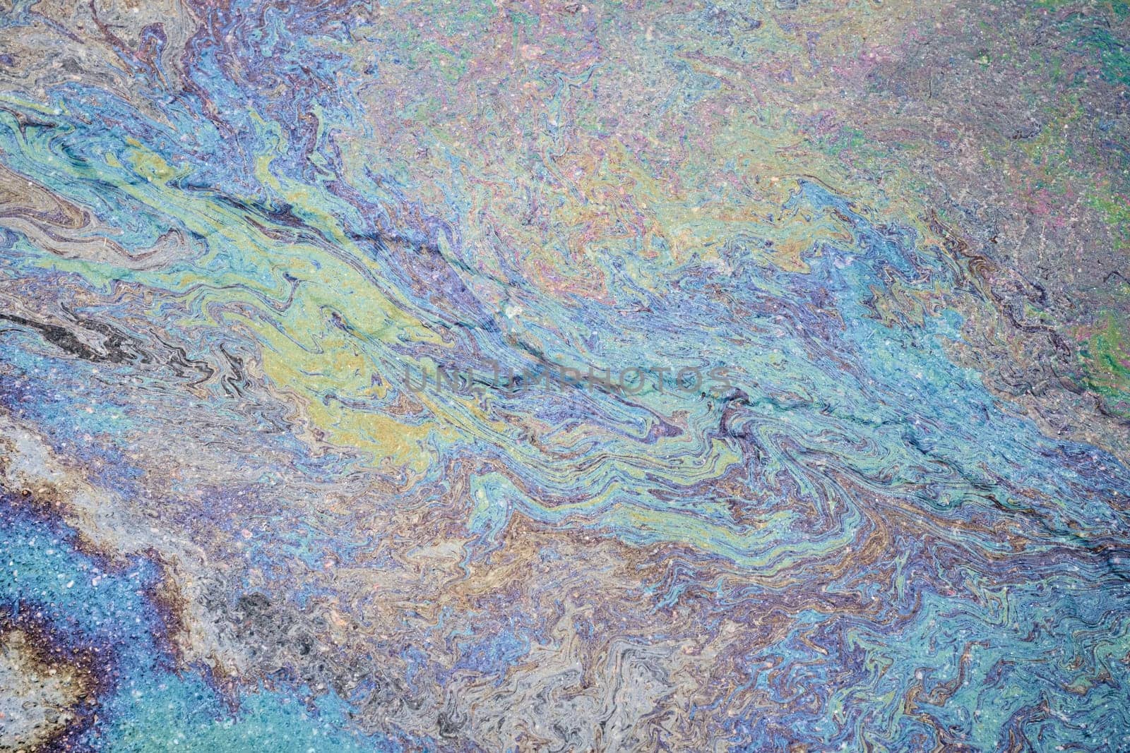 Colorful petrol oil spill creating a textured surface on the wet pavement.
