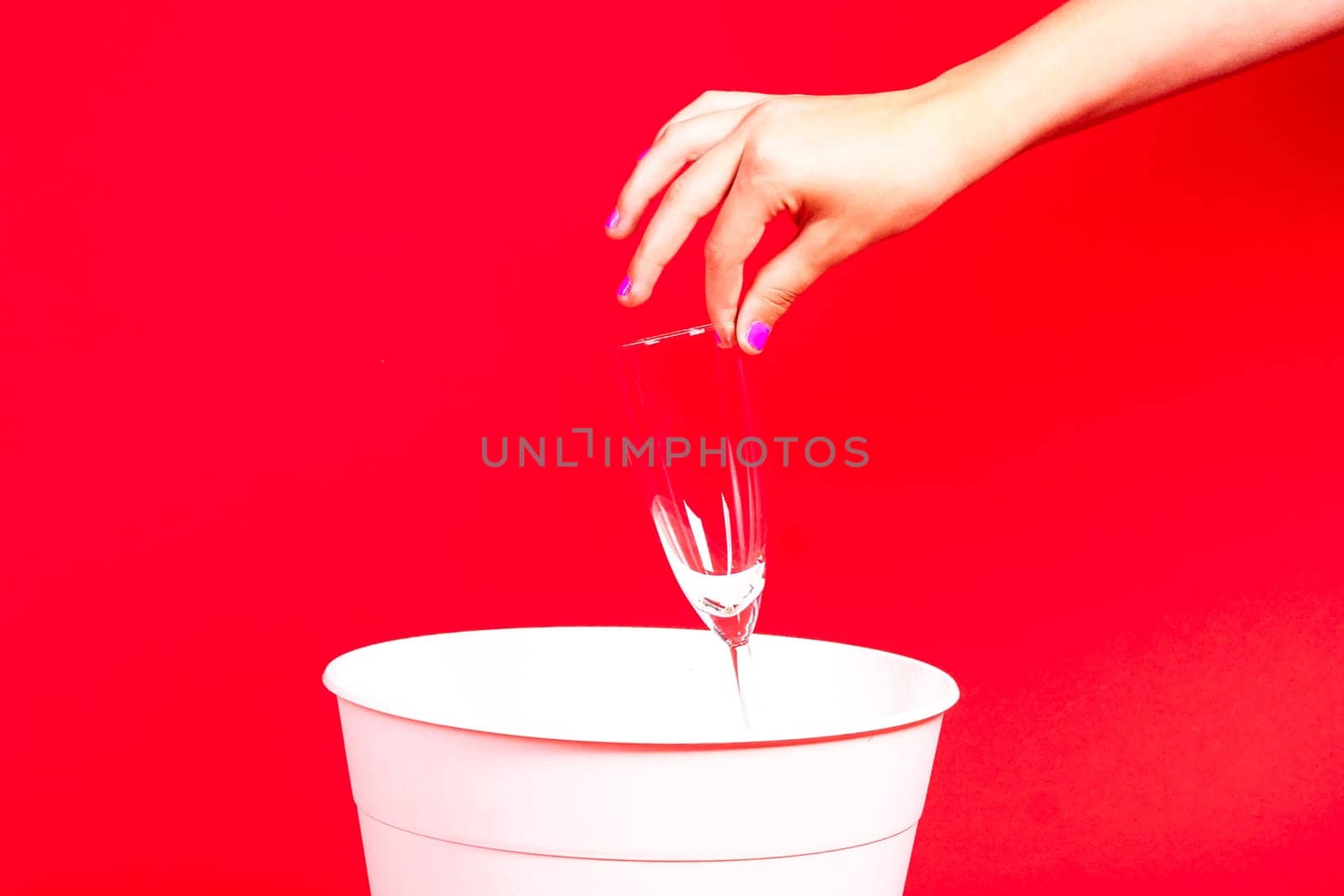 A woman is disposing of a cup in a trash can, making a gesture with her hand to pour out the liquid from the glass drinkware