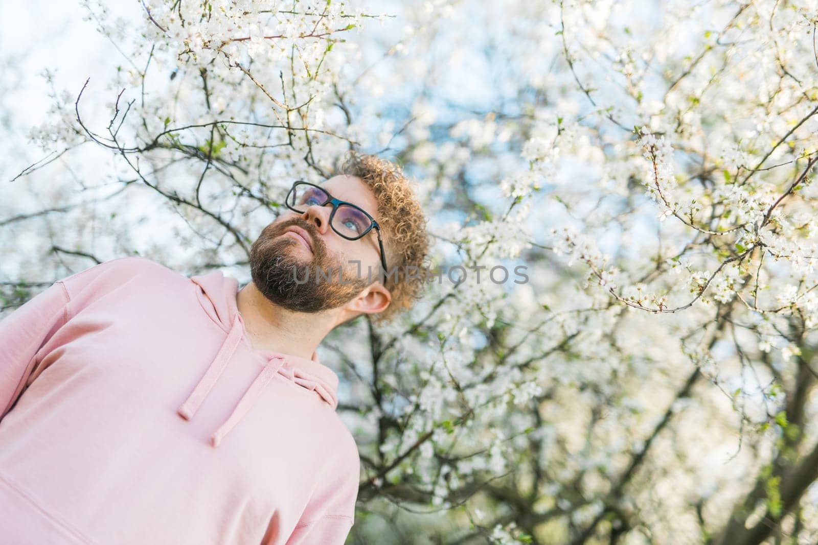 Handsome man outdoors portrait on background cherry blossoms or apple blossoms. Millennial generation guy and new masculinity concept. Copy space by Satura86